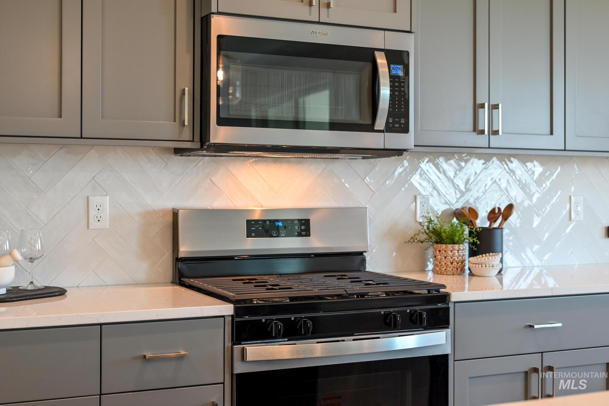 Kitchen with appliances with stainless steel finishes, gray cabinets, tasteful backsplash, and light stone counters