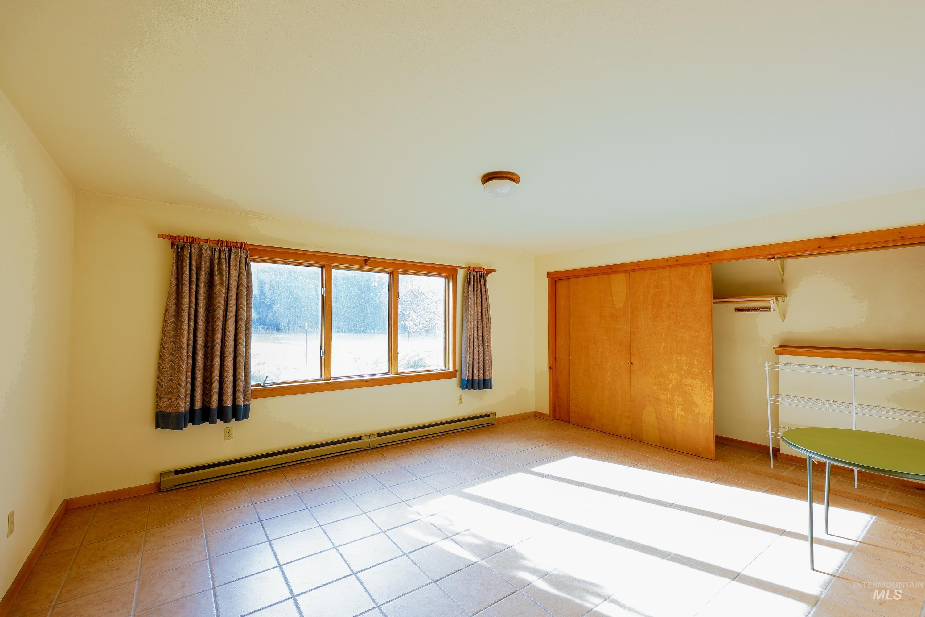 Unfurnished bedroom with baseboard heating, a closet, and light tile patterned flooring