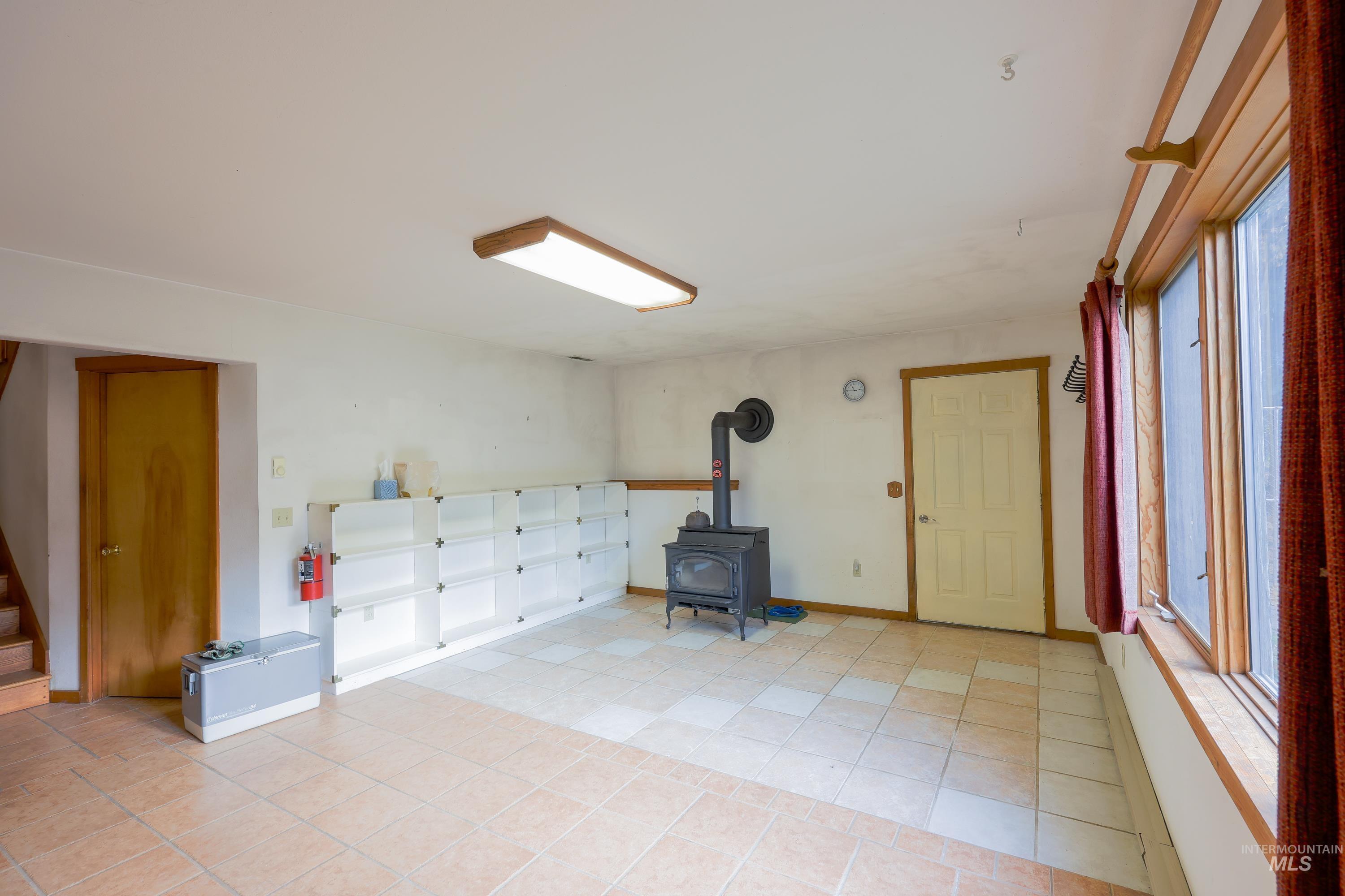 Basement with a wood stove, light tile patterned floors, and stairway