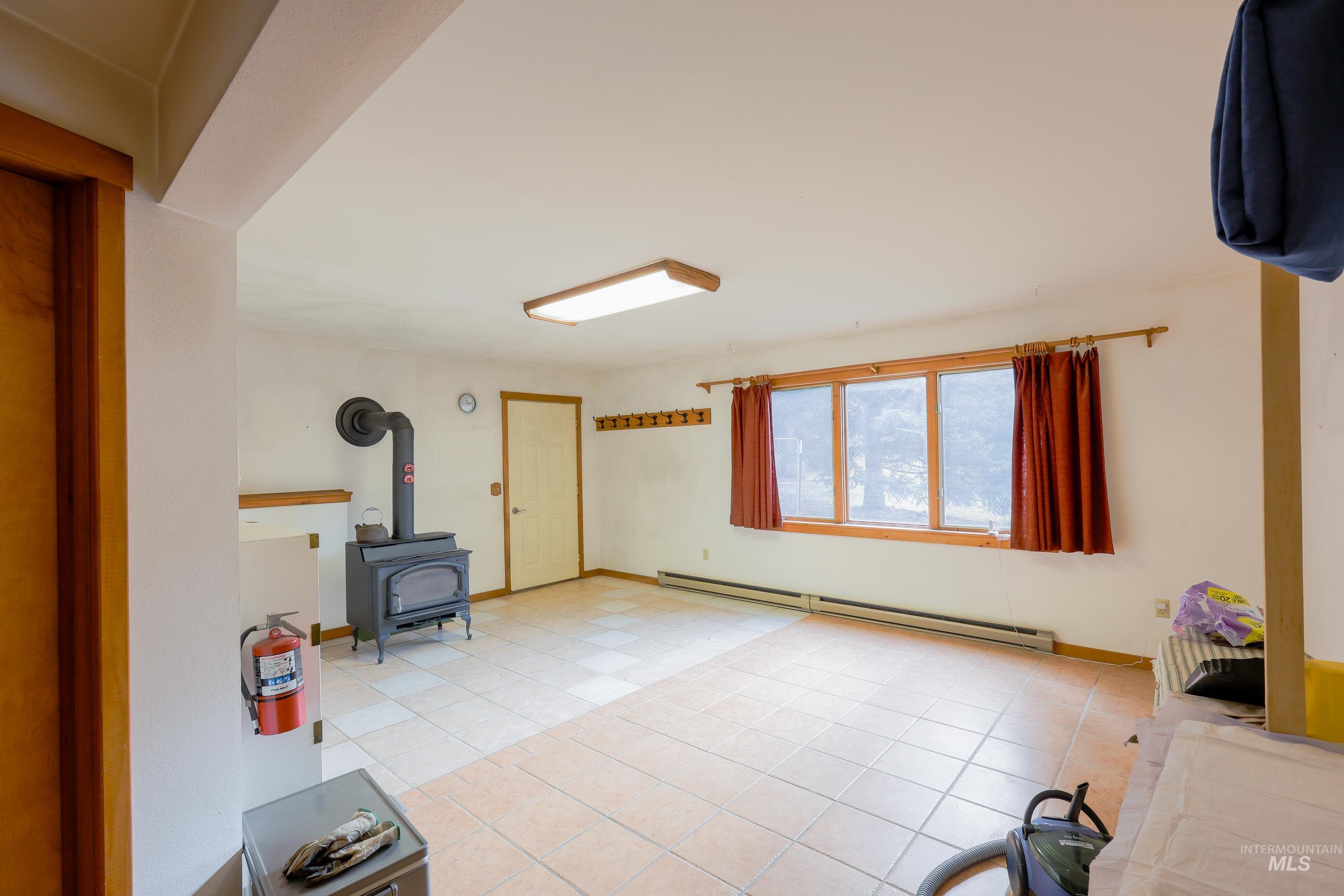 Interior space with a wood stove, baseboard heating, and light tile patterned floors