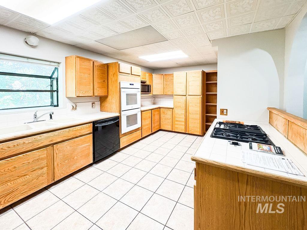 Kitchen featuring black appliances, tile countertops, light tile patterned floors, and light brown cabinetry