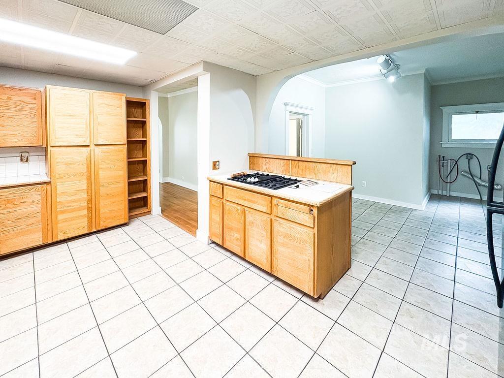 Kitchen featuring light countertops, gas cooktop, light tile patterned floors, light brown cabinetry, and crown molding