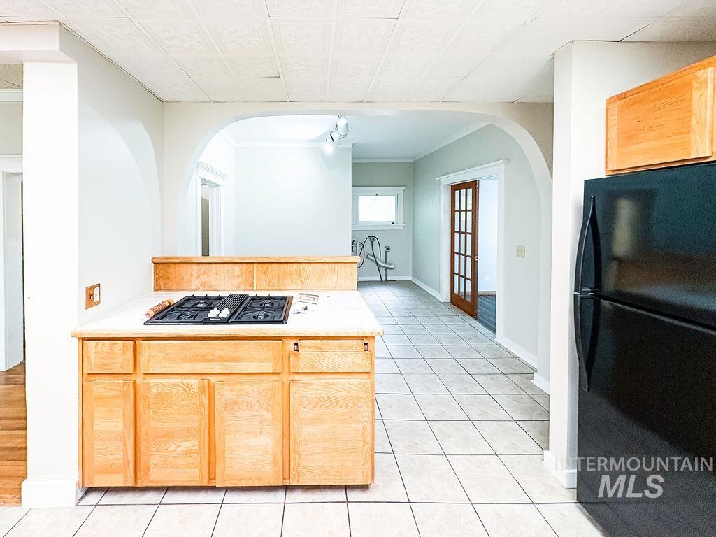 Kitchen featuring black appliances, arched walkways, light countertops, and light tile patterned floors