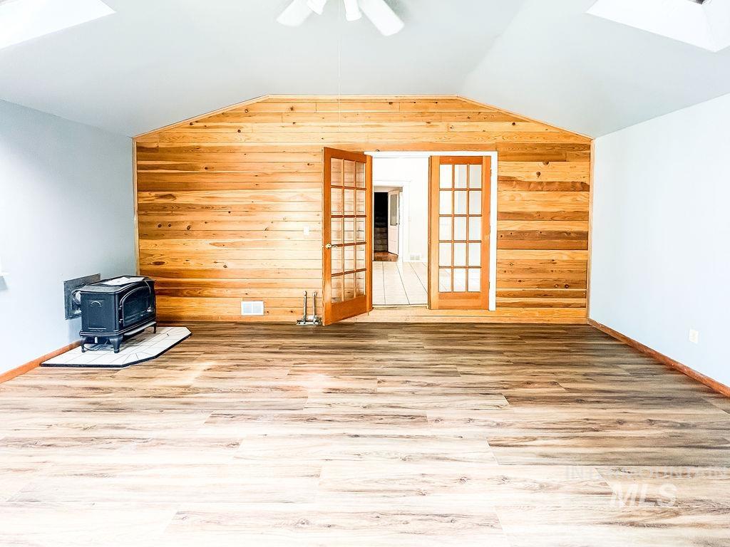 Additional living space featuring wooden walls, a wood stove, lofted ceiling, a skylight, and wood finished floors