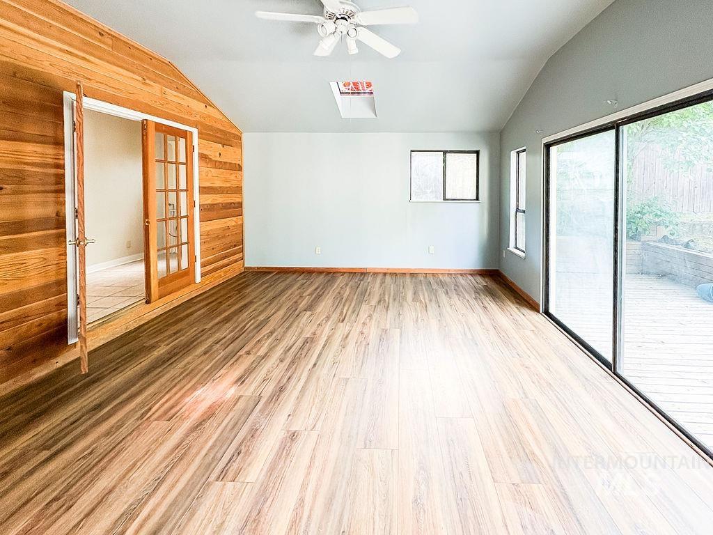 Empty room with vaulted ceiling, wood walls, a ceiling fan, healthy amount of natural light, and light wood-style flooring