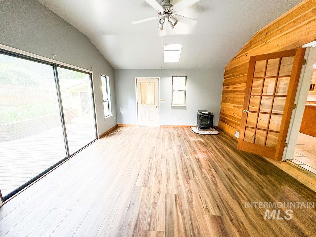 Unfurnished living room with lofted ceiling, a wood stove, wood finished floors, ceiling fan, and wooden walls