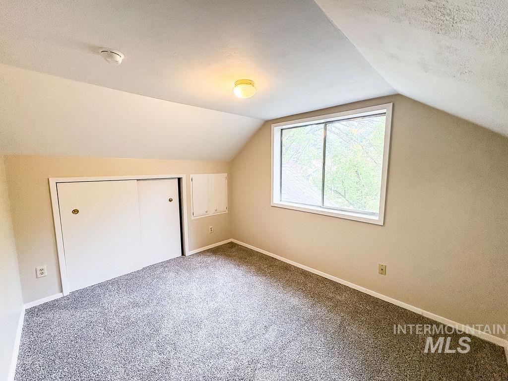 Additional living space featuring vaulted ceiling, carpet flooring, and a textured ceiling