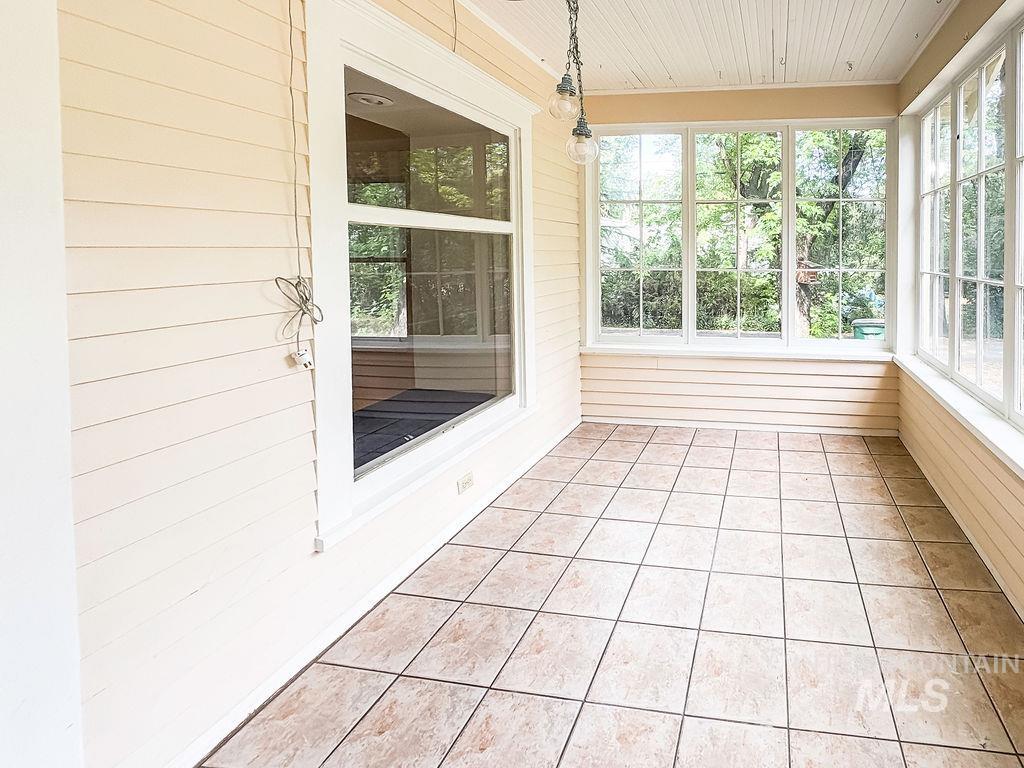 Unfurnished sunroom with wood walls, healthy amount of natural light, wood ceiling, and tile patterned flooring