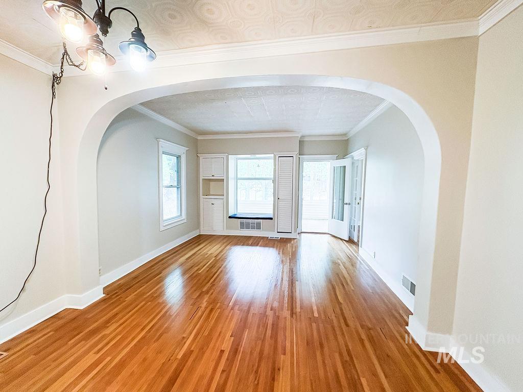 Unfurnished living room featuring arched walkways, light wood-type flooring, a chandelier, and ornamental molding