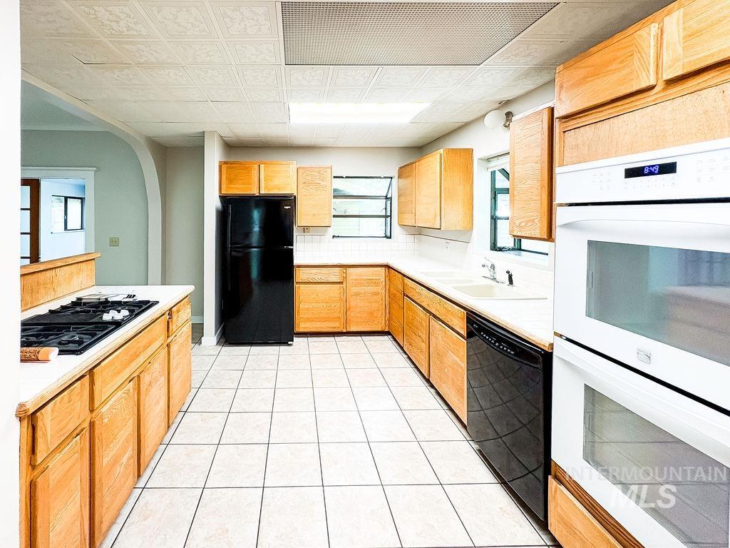 Kitchen with black appliances, light countertops, backsplash, arched walkways, and light tile patterned floors