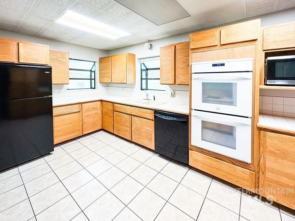 Kitchen featuring black appliances, light countertops, decorative backsplash, light brown cabinets, and light tile patterned floors