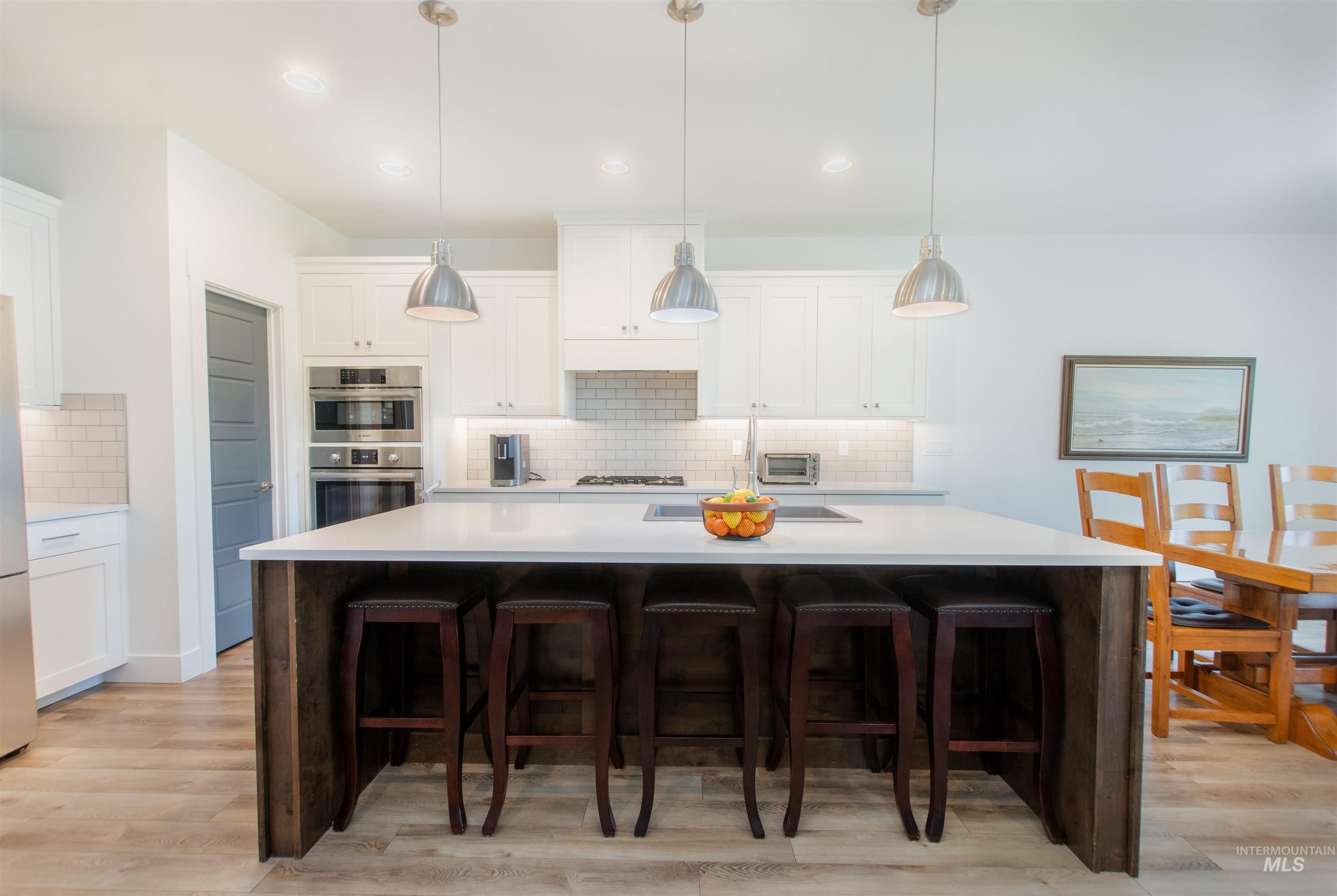 Kitchen featuring white cabinetry, an island with sink, tasteful backsplash, hanging light fixtures, and light wood-type flooring