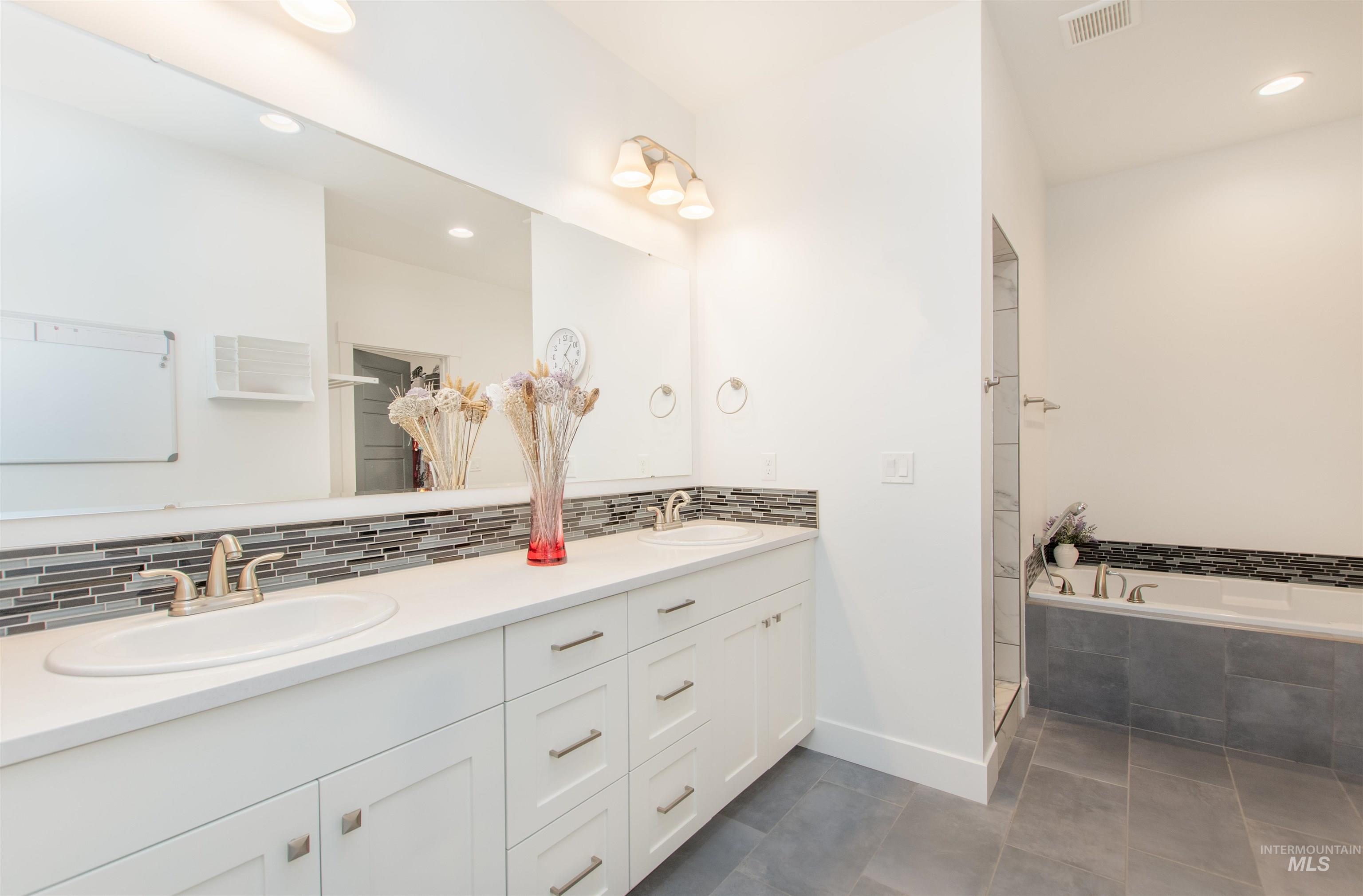 Full bath featuring double vanity, recessed lighting, a bath, decorative backsplash, and dark tile patterned flooring