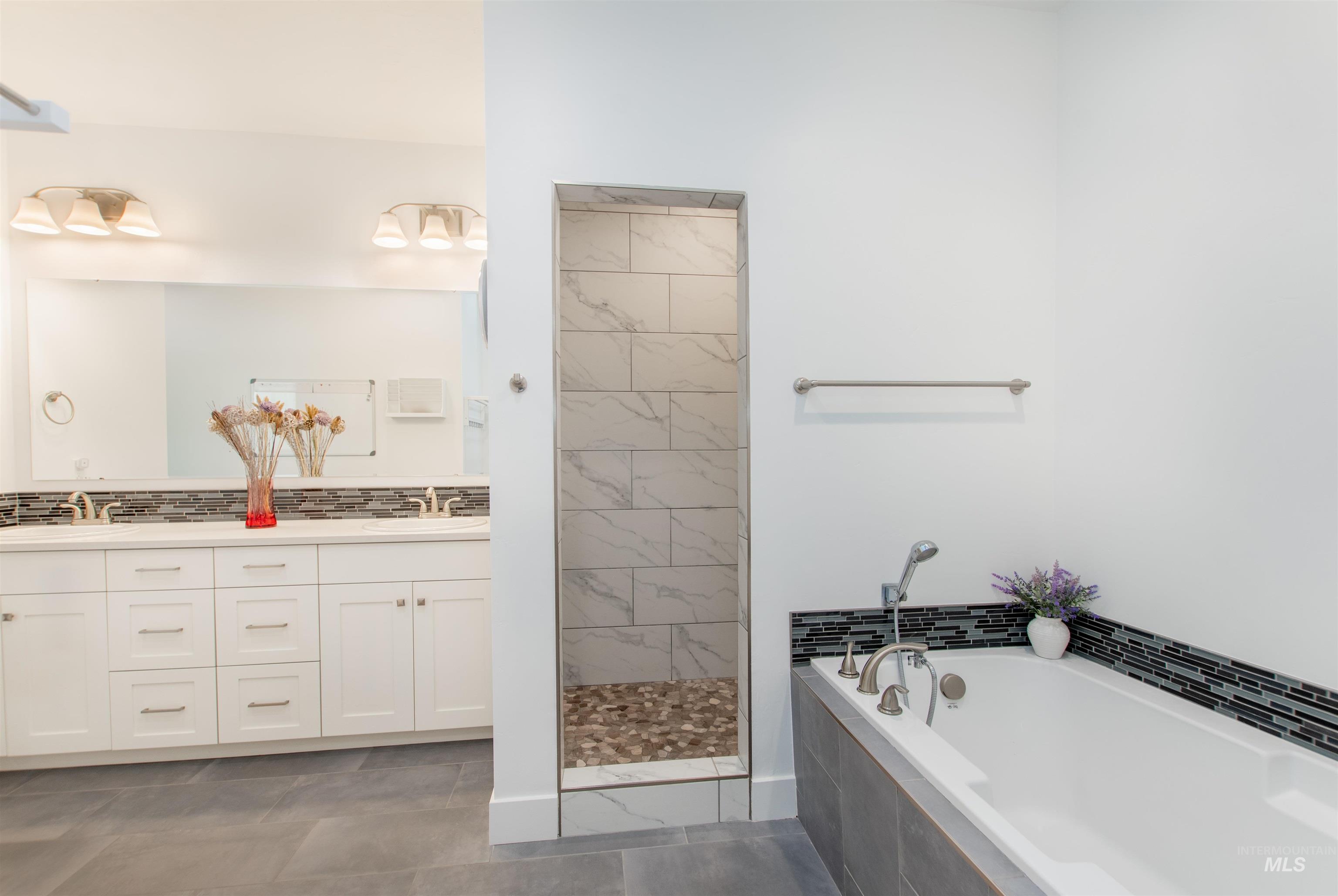 Bathroom featuring a bath, double vanity, decorative backsplash, walk in shower, and dark tile patterned flooring