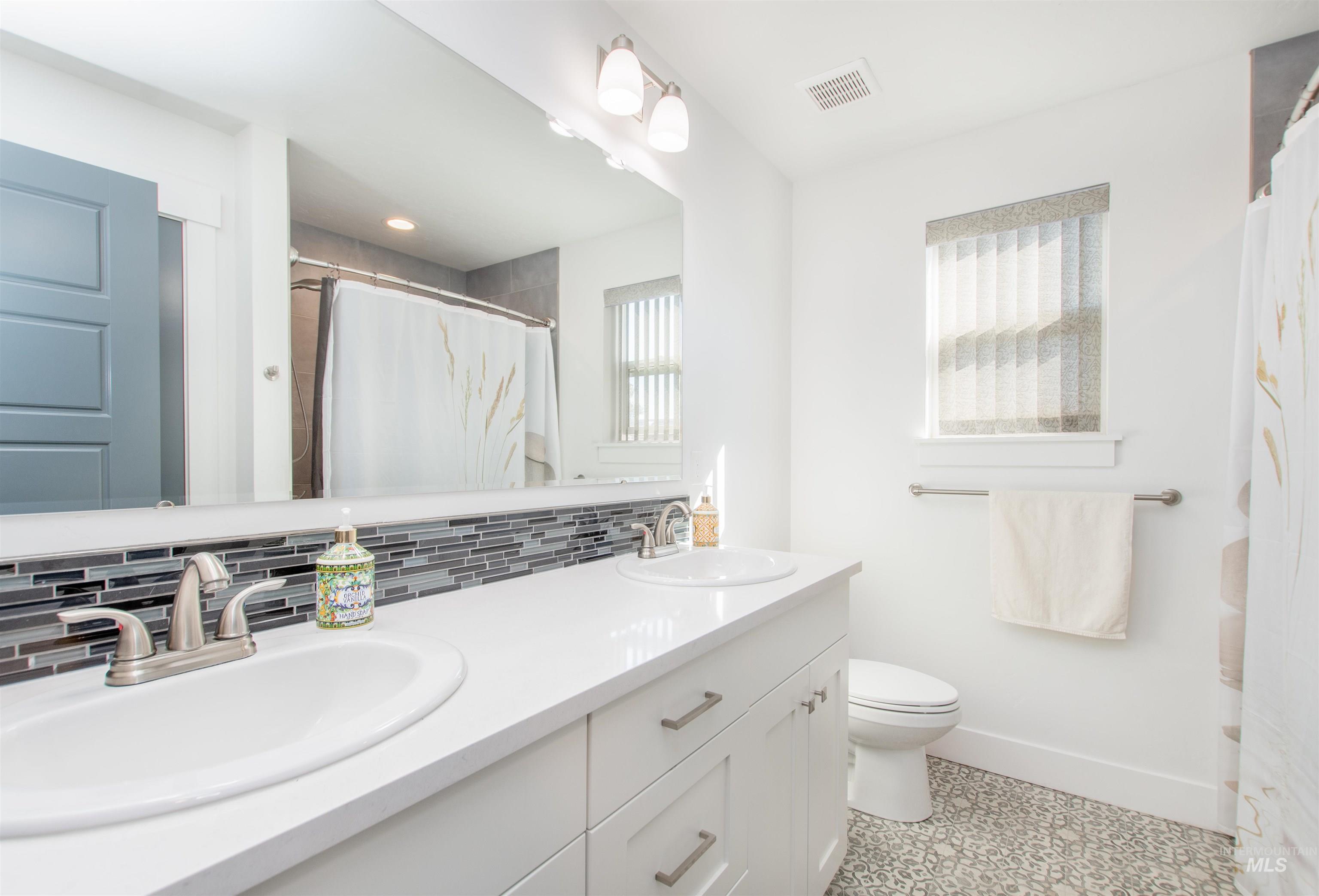 Bathroom with double vanity, backsplash, curtained shower, and light tile patterned floors
