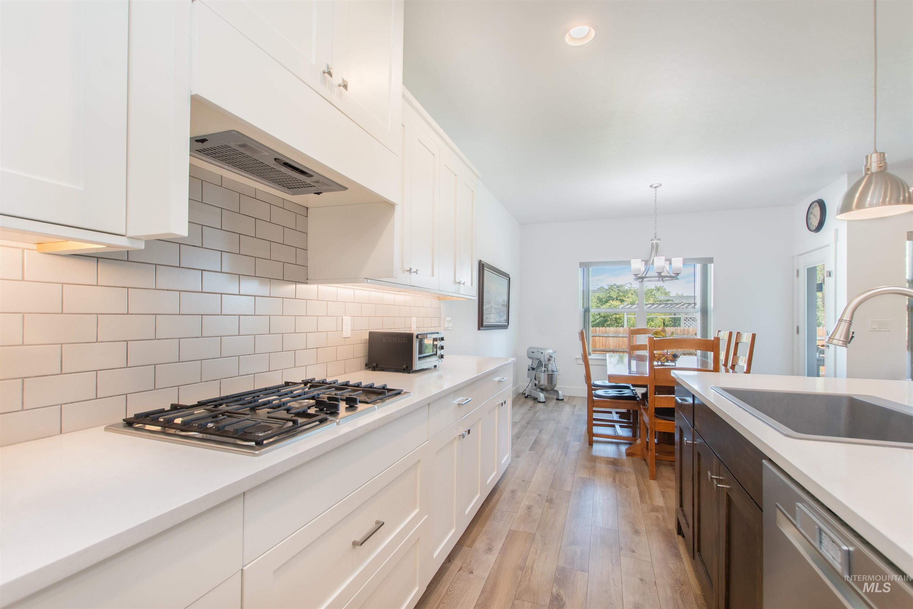 Kitchen featuring white cabinets, hanging light fixtures, appliances with stainless steel finishes, light wood-style floors, and decorative backsplash