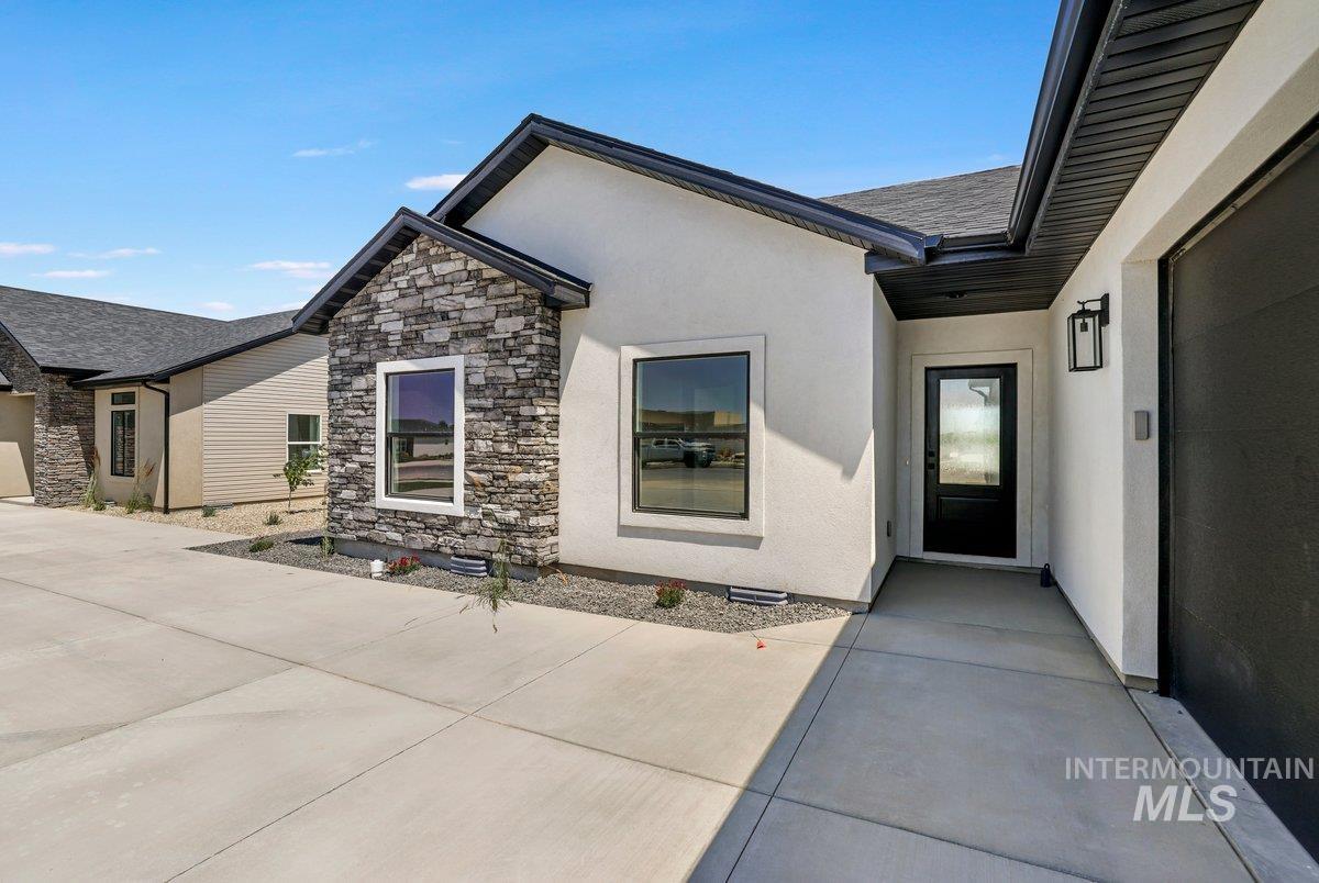 Entrance to property with stucco siding, stone siding, and a patio