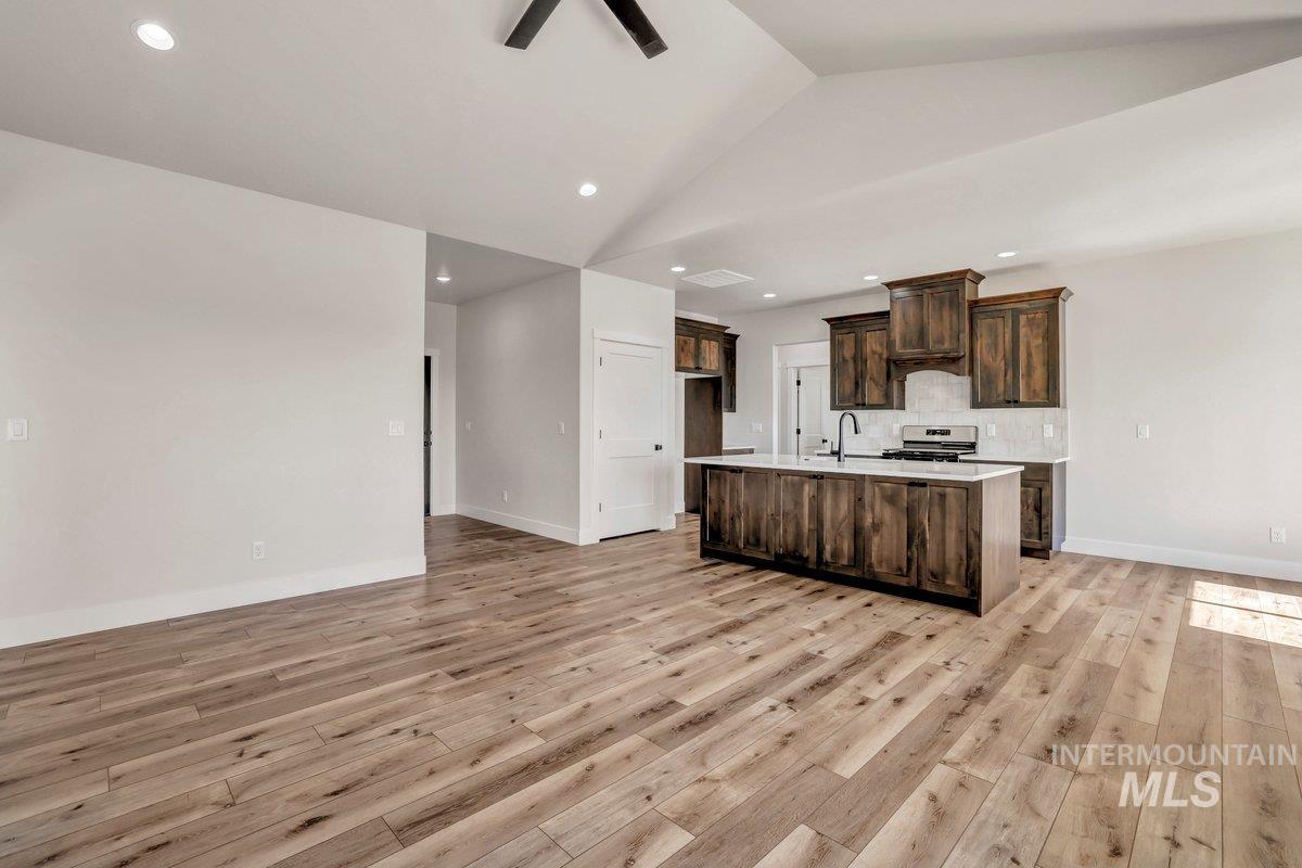 Kitchen with light wood finished floors, an island with sink, dark brown cabinetry, decorative backsplash, and light countertops