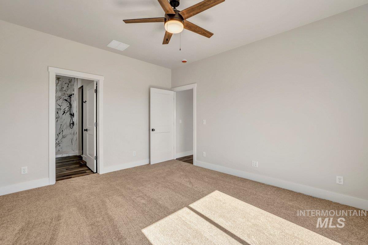 Unfurnished bedroom featuring carpet flooring, ensuite bathroom, and a ceiling fan