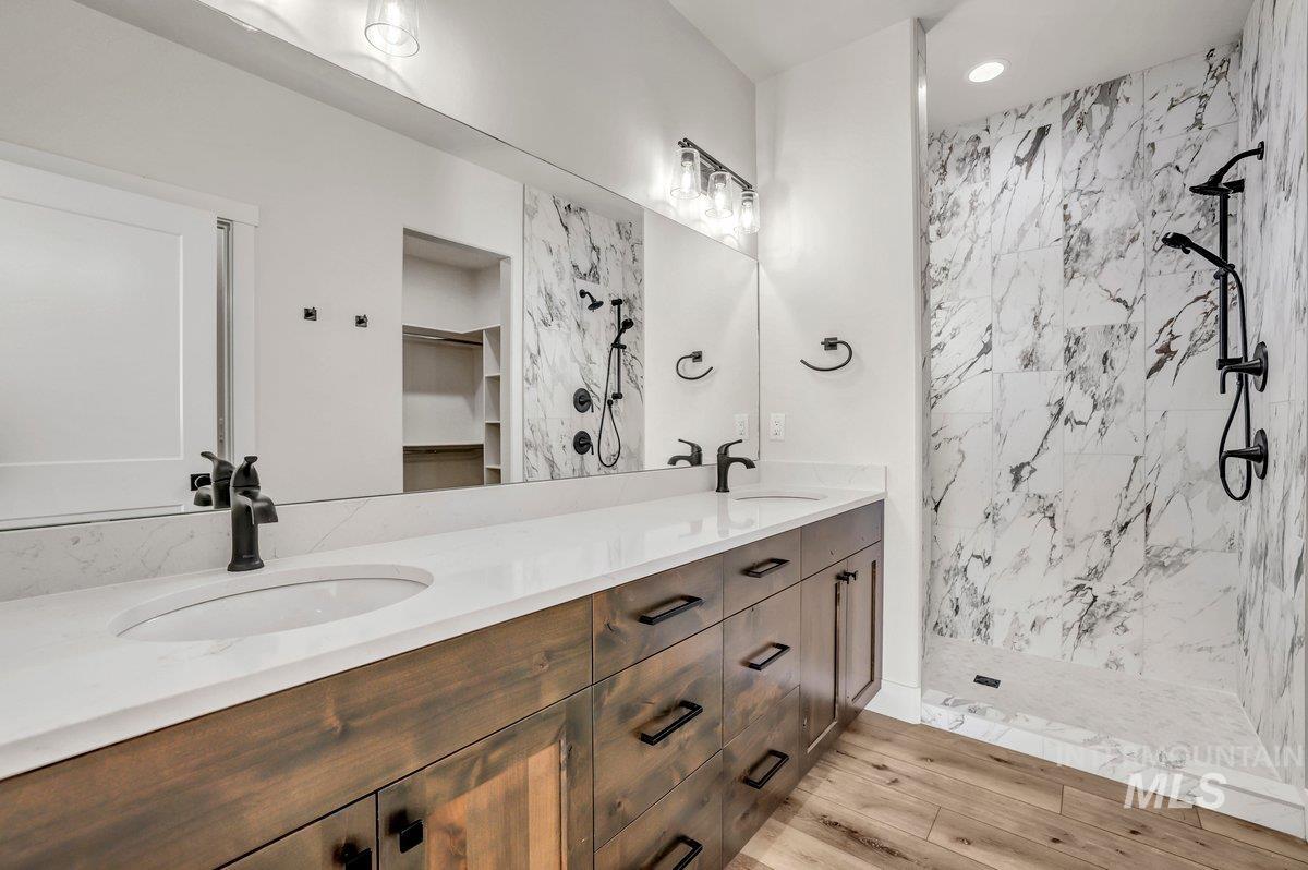 Bathroom featuring double vanity, a tile shower, a spacious closet, wood finished floors, and recessed lighting