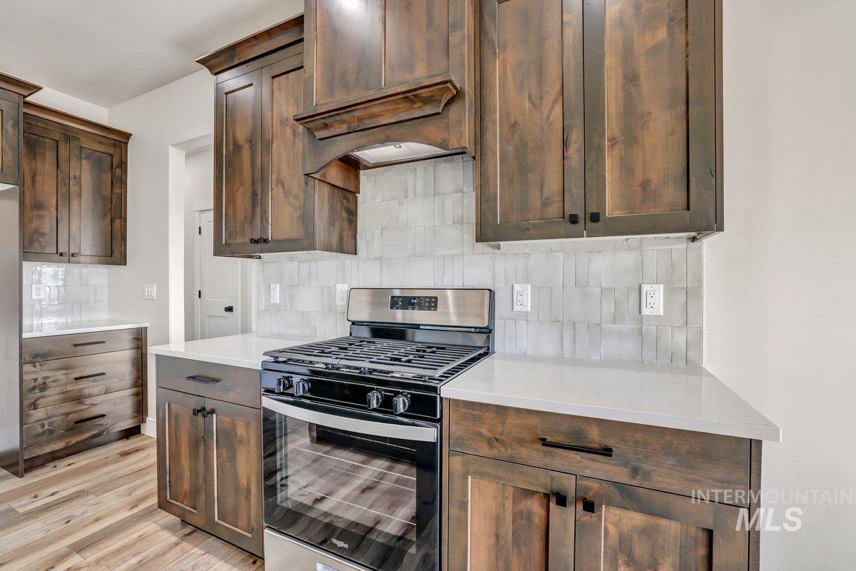 Kitchen with stainless steel gas range oven, tasteful backsplash, exhaust hood, and light countertops