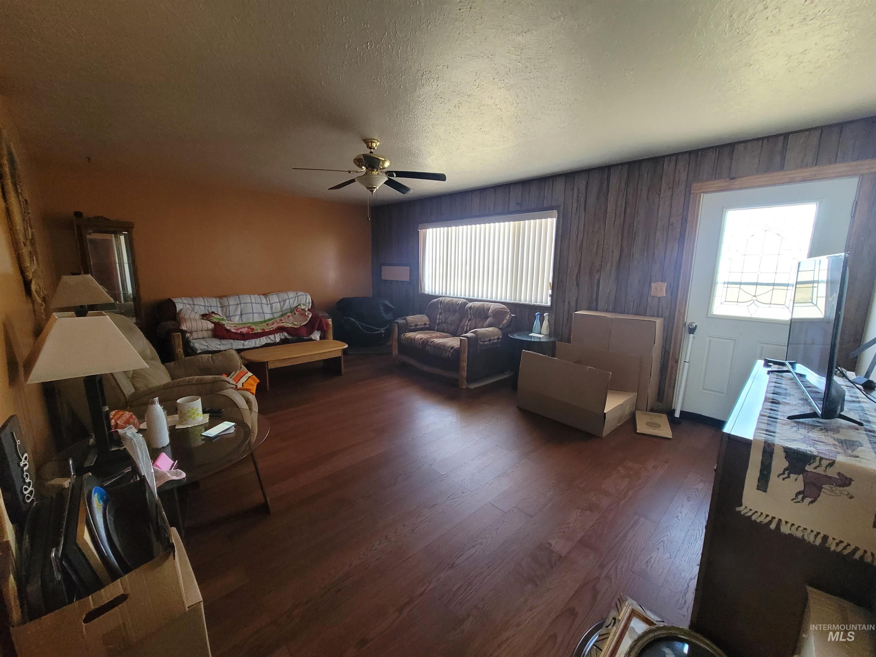 Living room featuring a textured ceiling, dark wood-type flooring, a ceiling fan, and wood walls