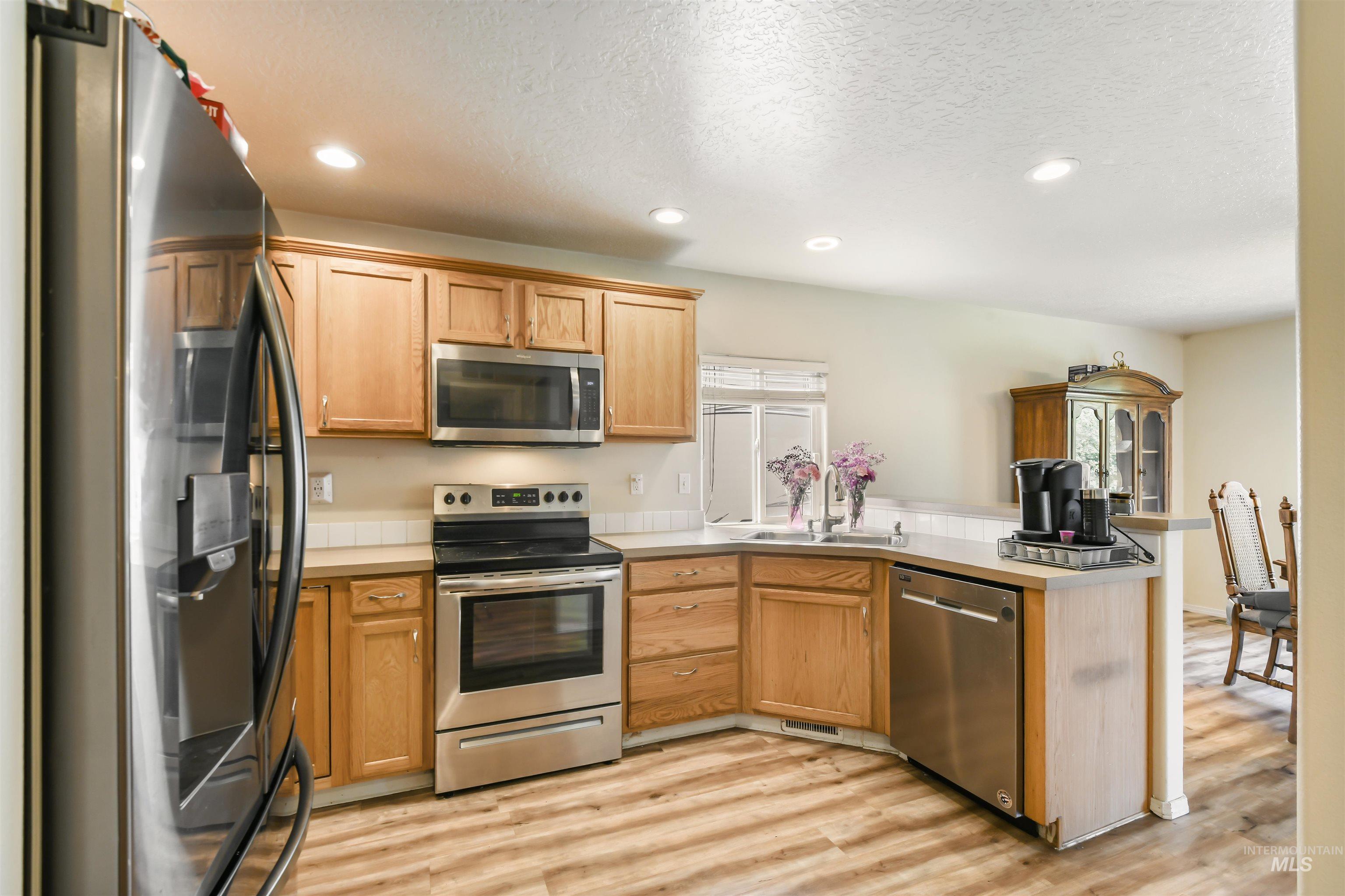 Kitchen featuring stainless steel appliances, a peninsula, light wood-style flooring, light countertops, and recessed lighting