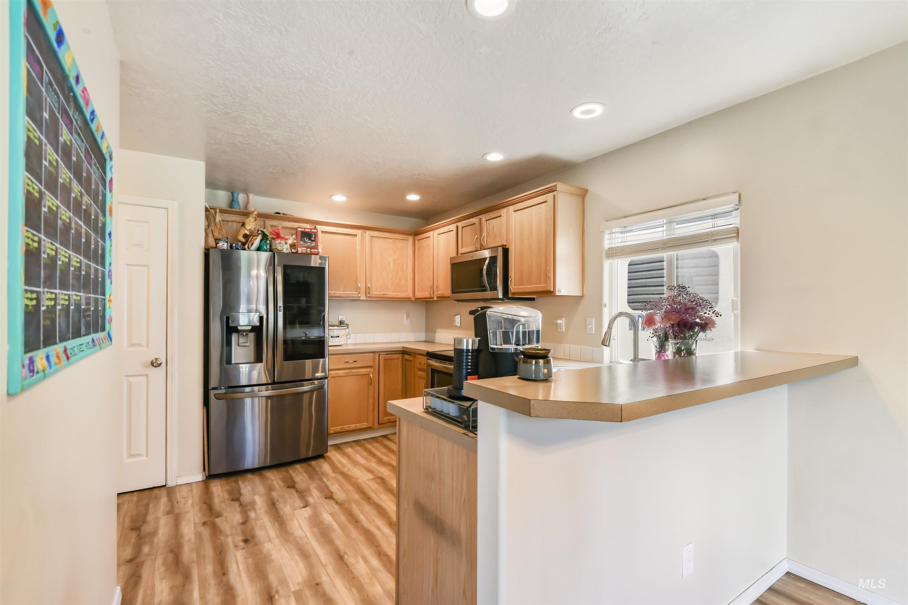 Kitchen with appliances with stainless steel finishes, a peninsula, light wood finished floors, light brown cabinetry, and recessed lighting