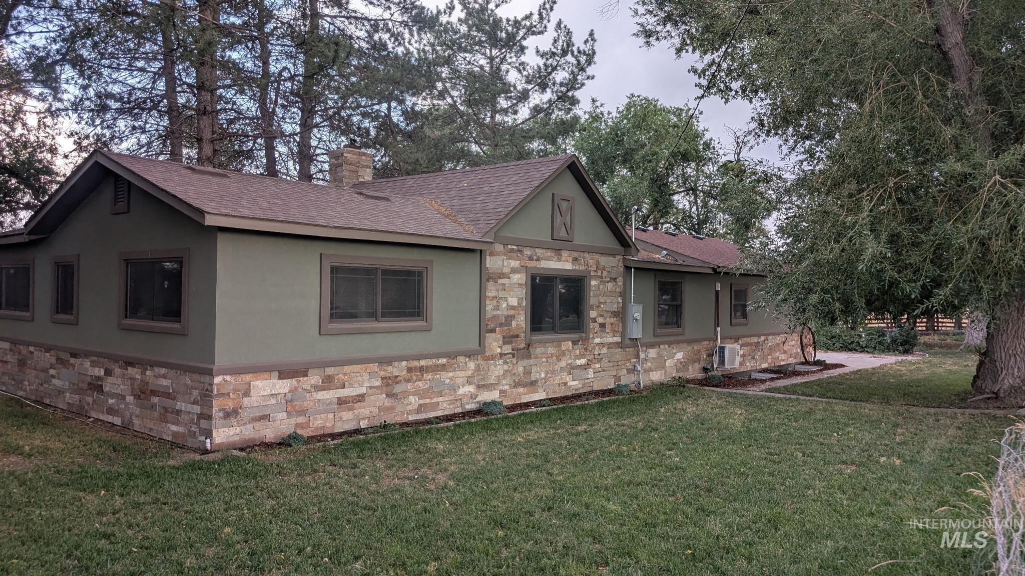 View of side of property featuring stone siding, a lawn, roof with shingles, stucco siding, and a chimney