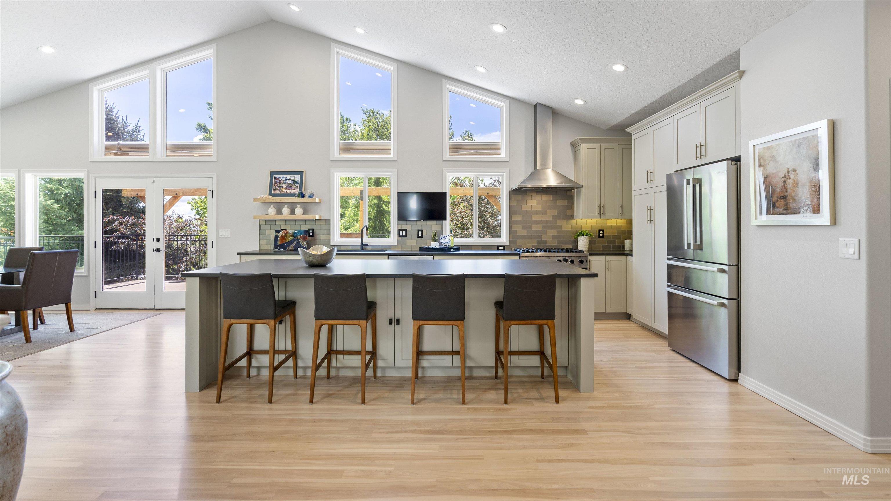 Kitchen featuring wall chimney range hood, freestanding refrigerator, dark countertops, a kitchen island, and high vaulted ceiling