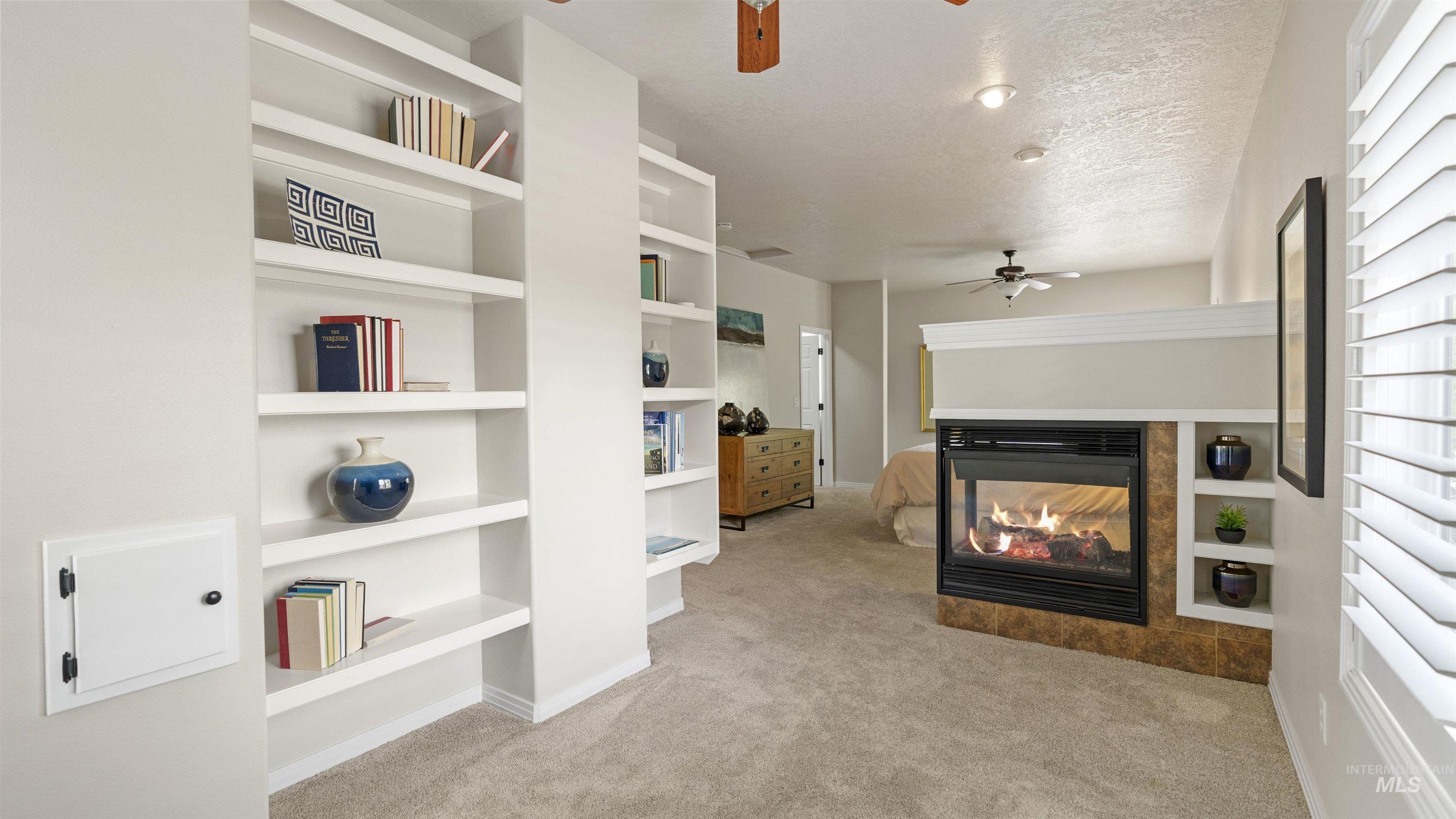 Living area featuring a ceiling fan, carpet, a multi sided fireplace, a textured ceiling, and built in features