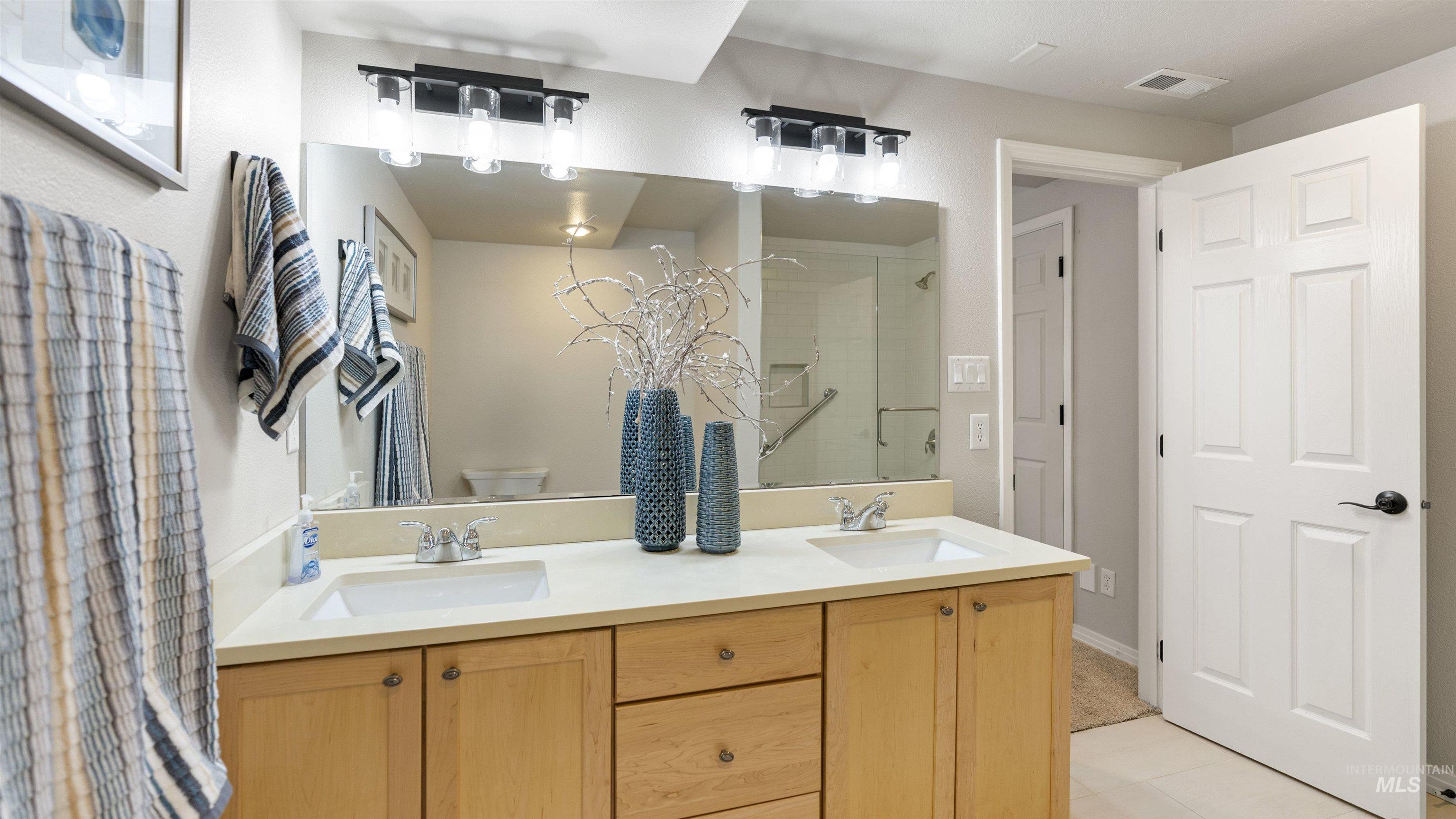 Full bathroom with a shower with door, double vanity, and tile patterned flooring