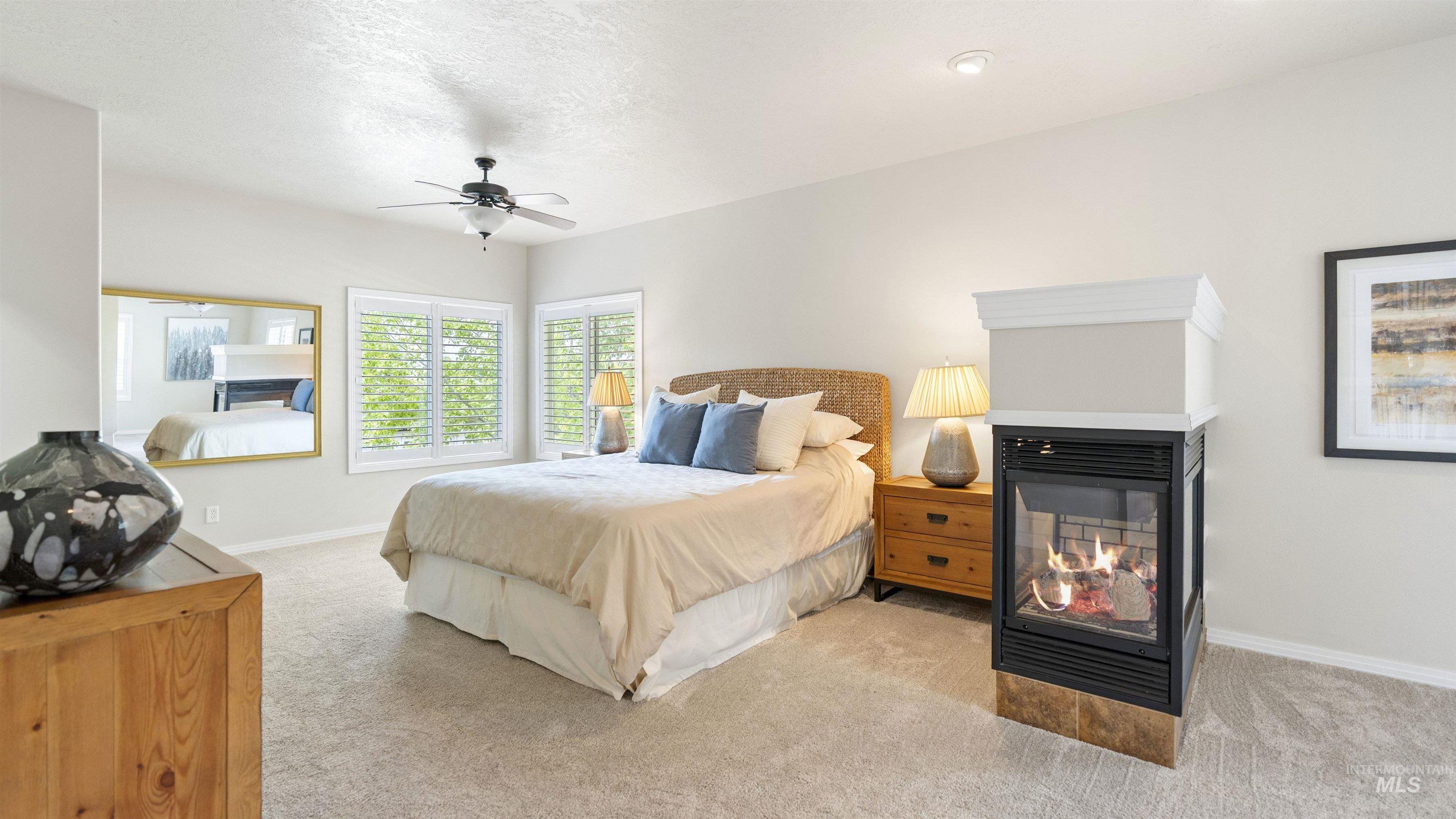 Carpeted bedroom with a multi sided fireplace and a ceiling fan