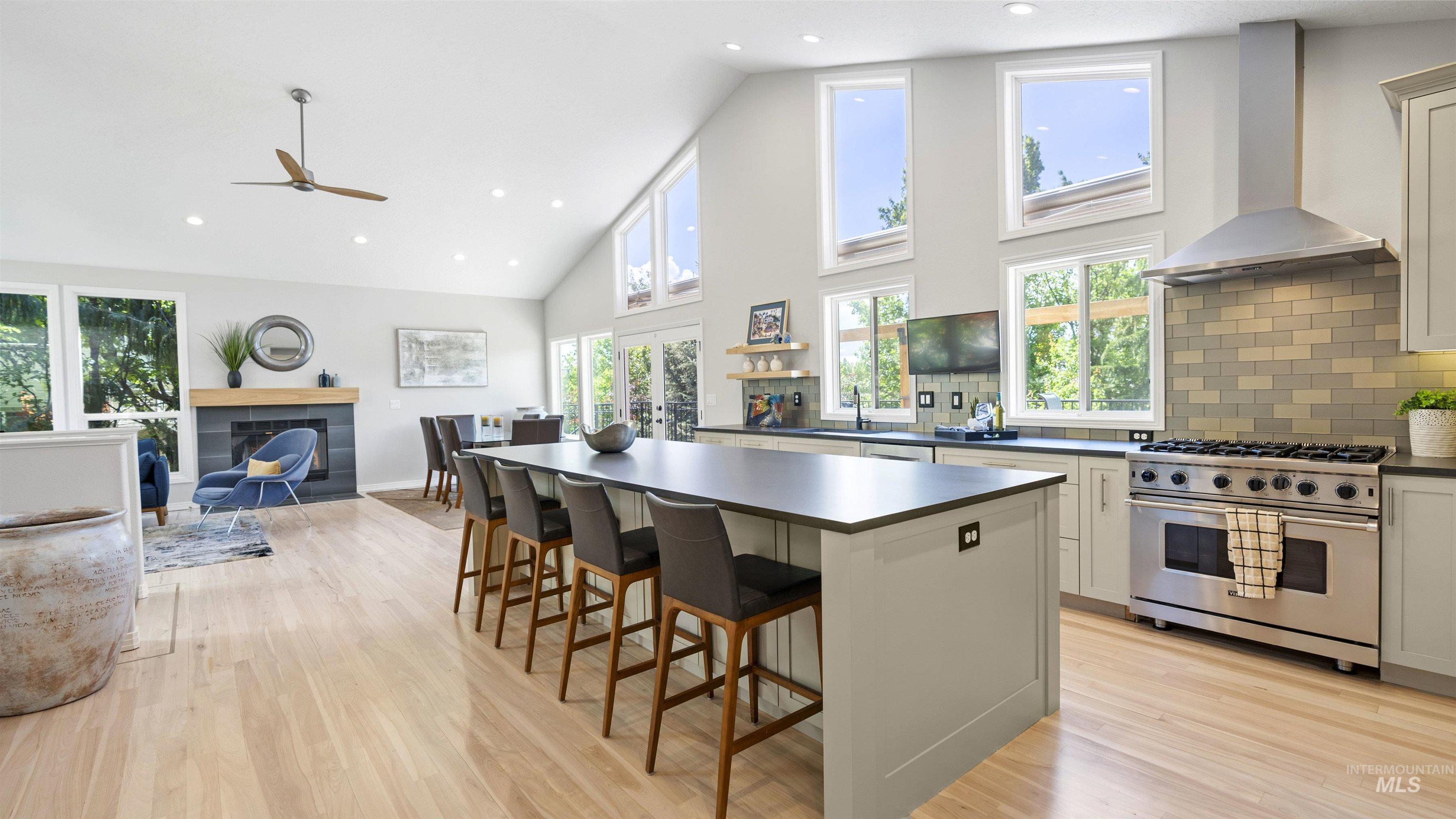Kitchen featuring high end range, wall chimney exhaust hood, dark countertops, light wood finished floors, and high vaulted ceiling