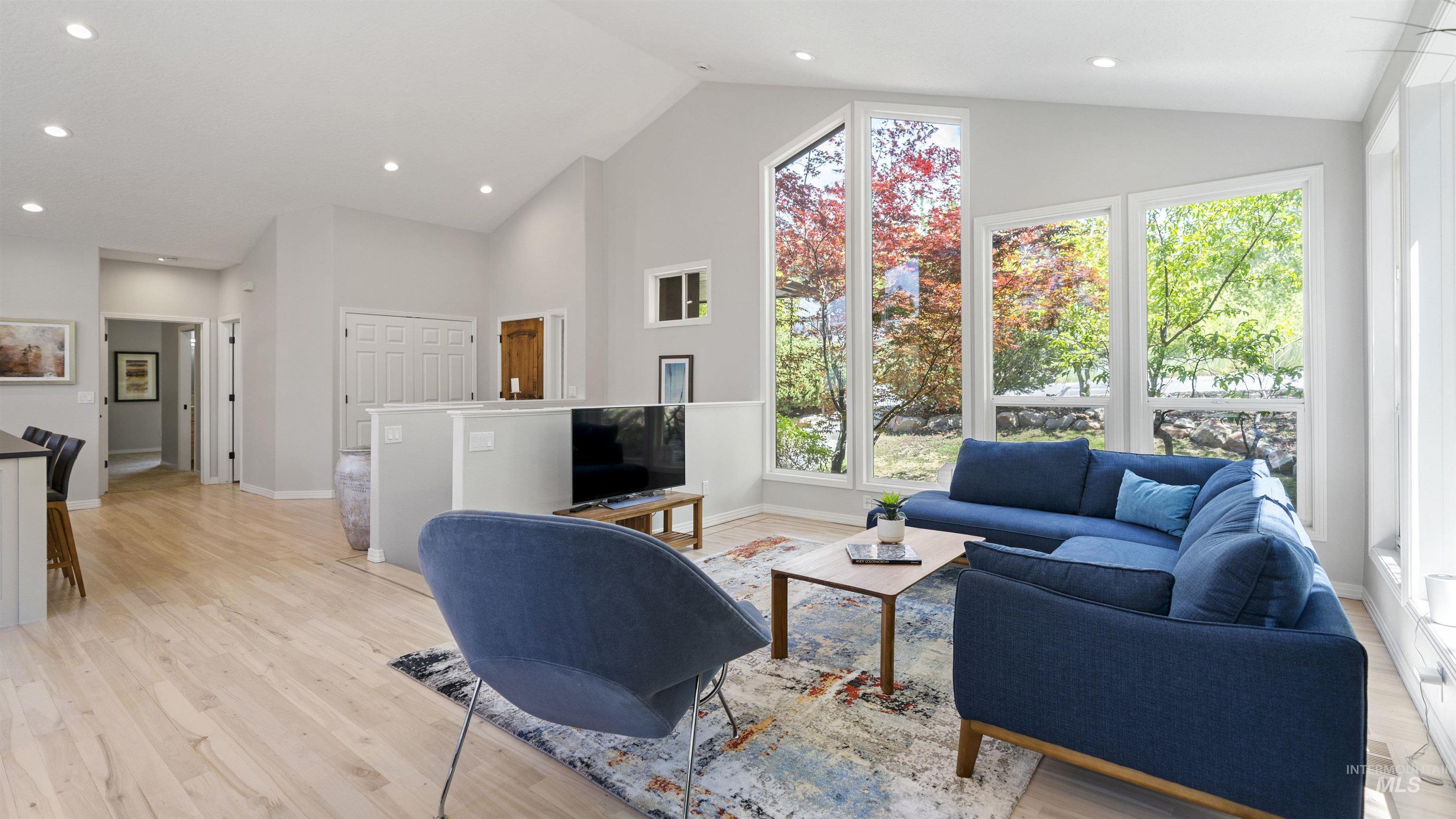 Living area with plenty of natural light, light wood-style flooring, high vaulted ceiling, and recessed lighting