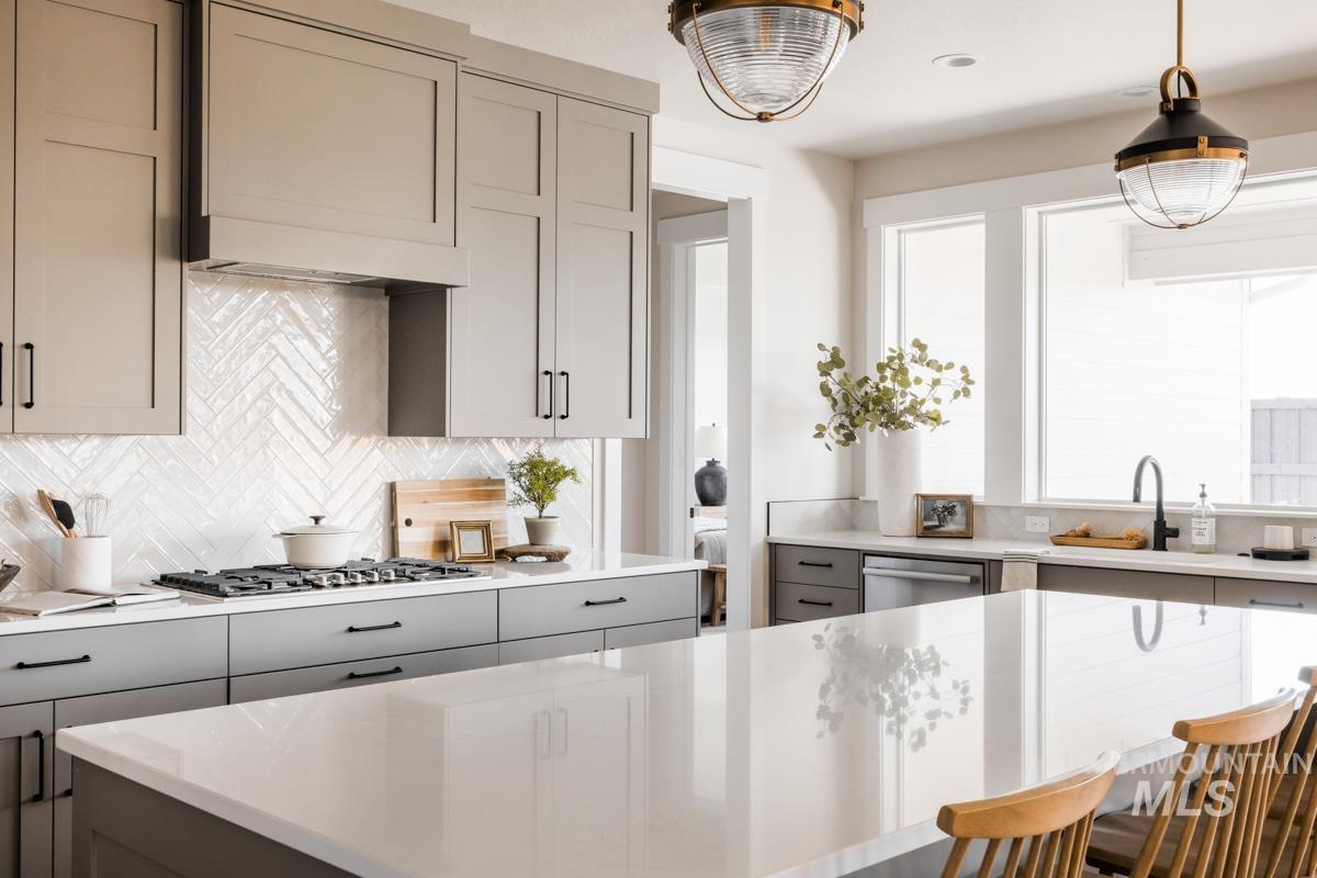 Kitchen with gray cabinetry, decorative backsplash, hanging light fixtures, and stainless steel appliances