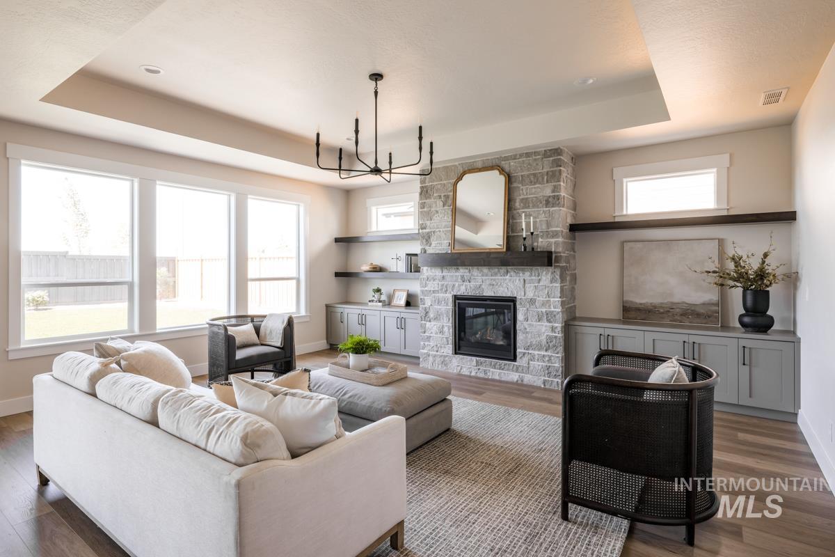 Living area with a tray ceiling, a chandelier, wood finished floors, and healthy amount of natural light