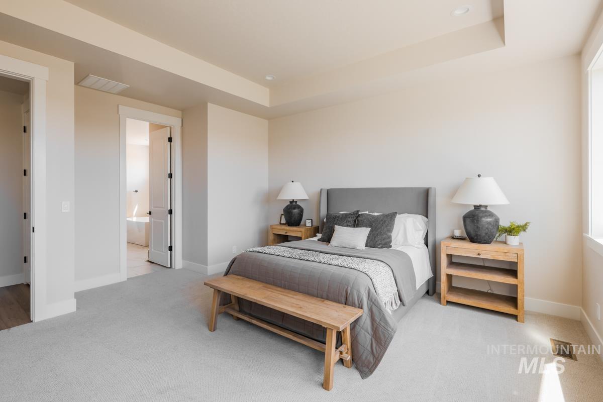 Bedroom with carpet flooring, a raised ceiling, and connected bathroom