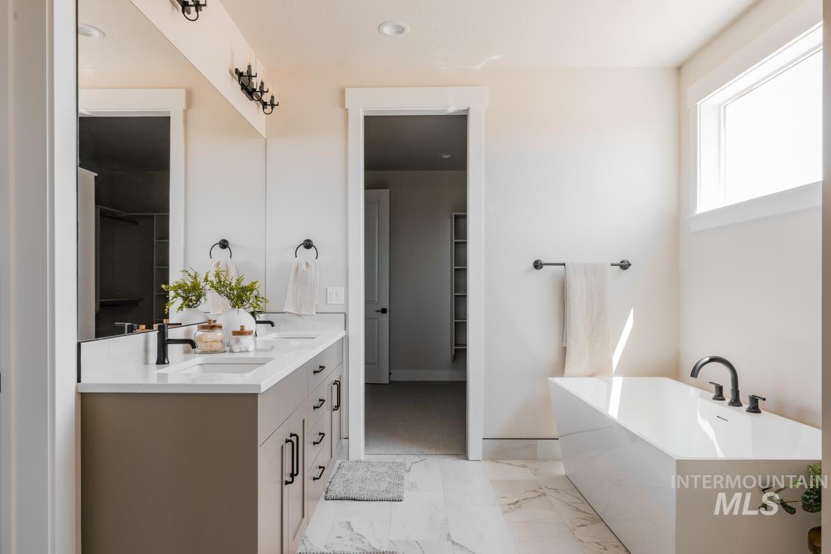 Bathroom featuring double vanity, a freestanding bath, marble finish flooring, and a spacious closet