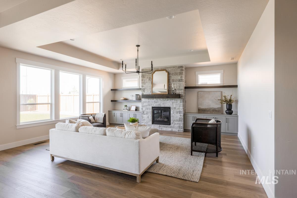 Living area with a raised ceiling, wood finished floors, a chandelier, and a stone fireplace