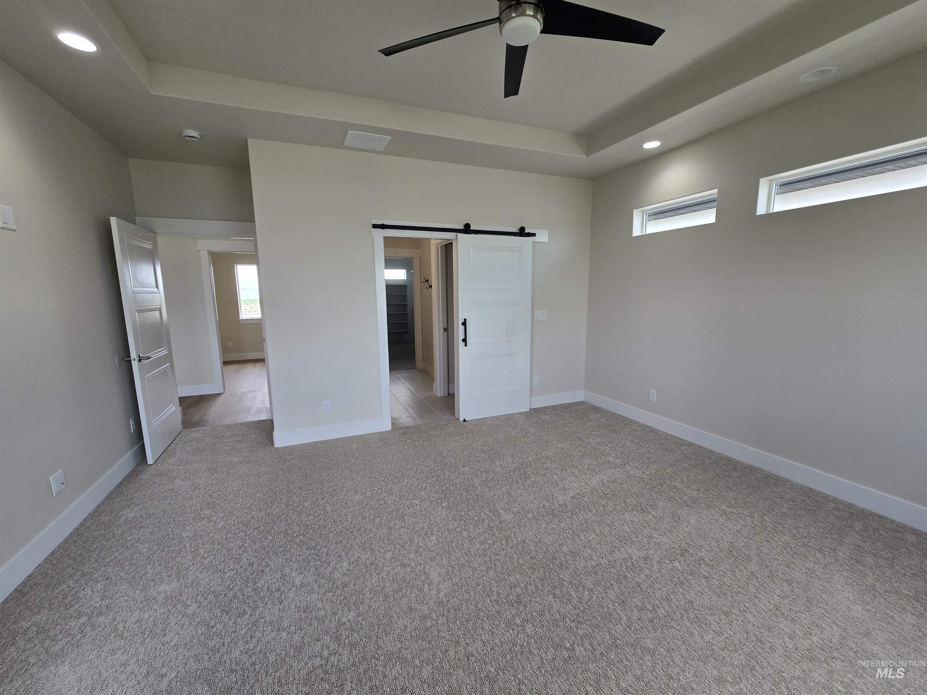 Unfurnished bedroom with light carpet, recessed lighting, a barn door, a raised ceiling, and ceiling fan