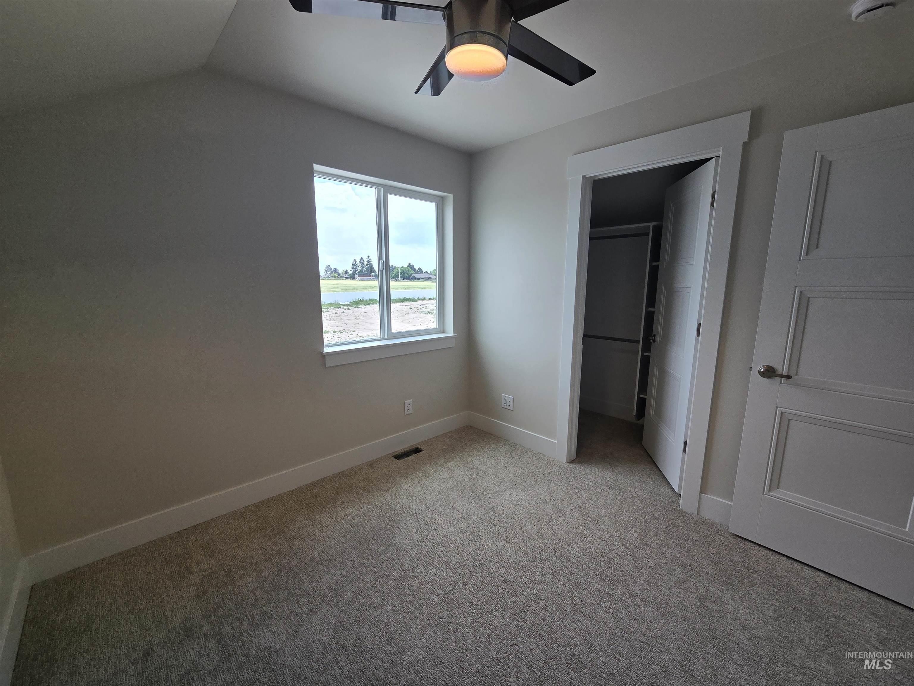 Unfurnished bedroom with light colored carpet, a walk in closet, a closet, a ceiling fan, and lofted ceiling