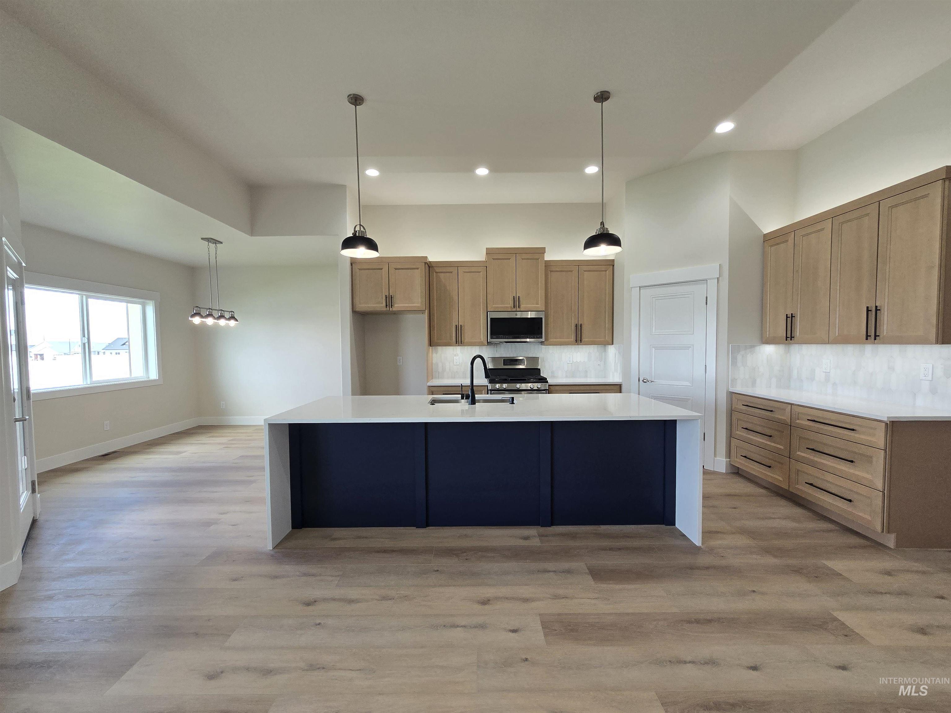 Kitchen featuring appliances with stainless steel finishes, backsplash, recessed lighting, light countertops, and an island with sink