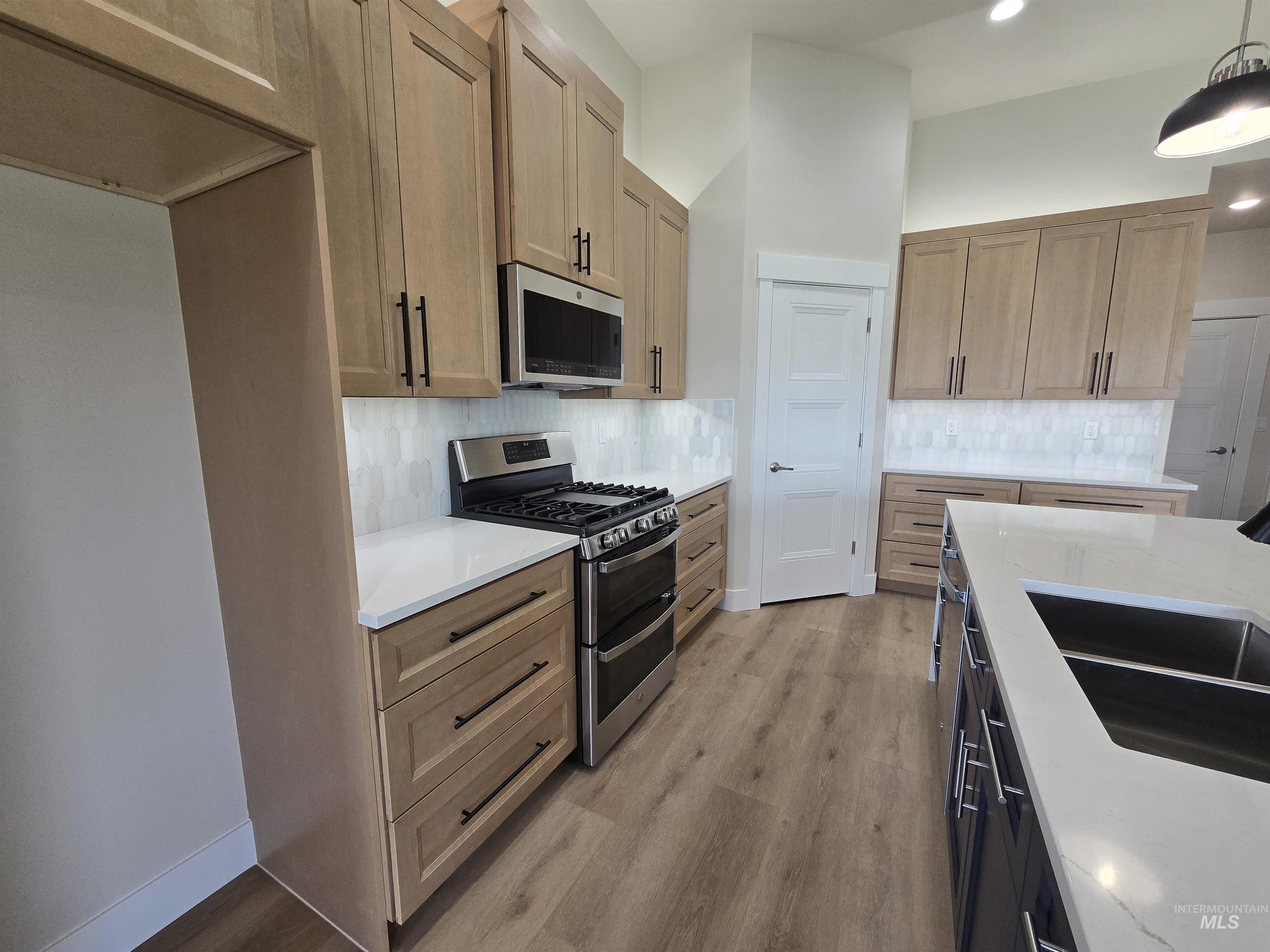 Kitchen featuring stainless steel appliances, light wood-style flooring, tasteful backsplash, recessed lighting, and hanging light fixtures