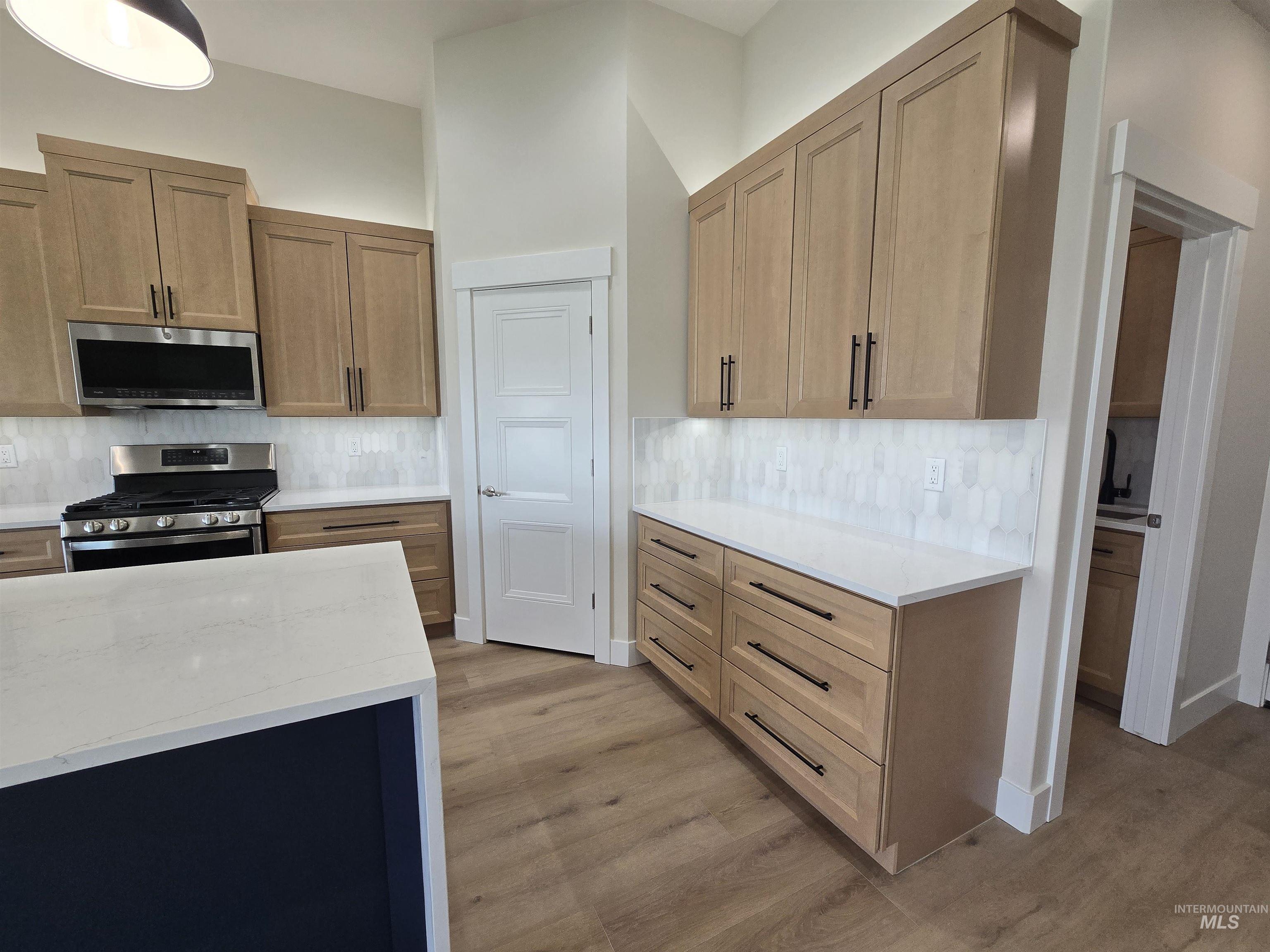 Kitchen featuring appliances with stainless steel finishes, light wood finished floors, backsplash, and light stone countertops