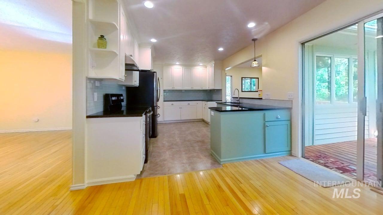 Kitchen with open shelves, dark countertops, light wood-style floors, white cabinets, and decorative backsplash