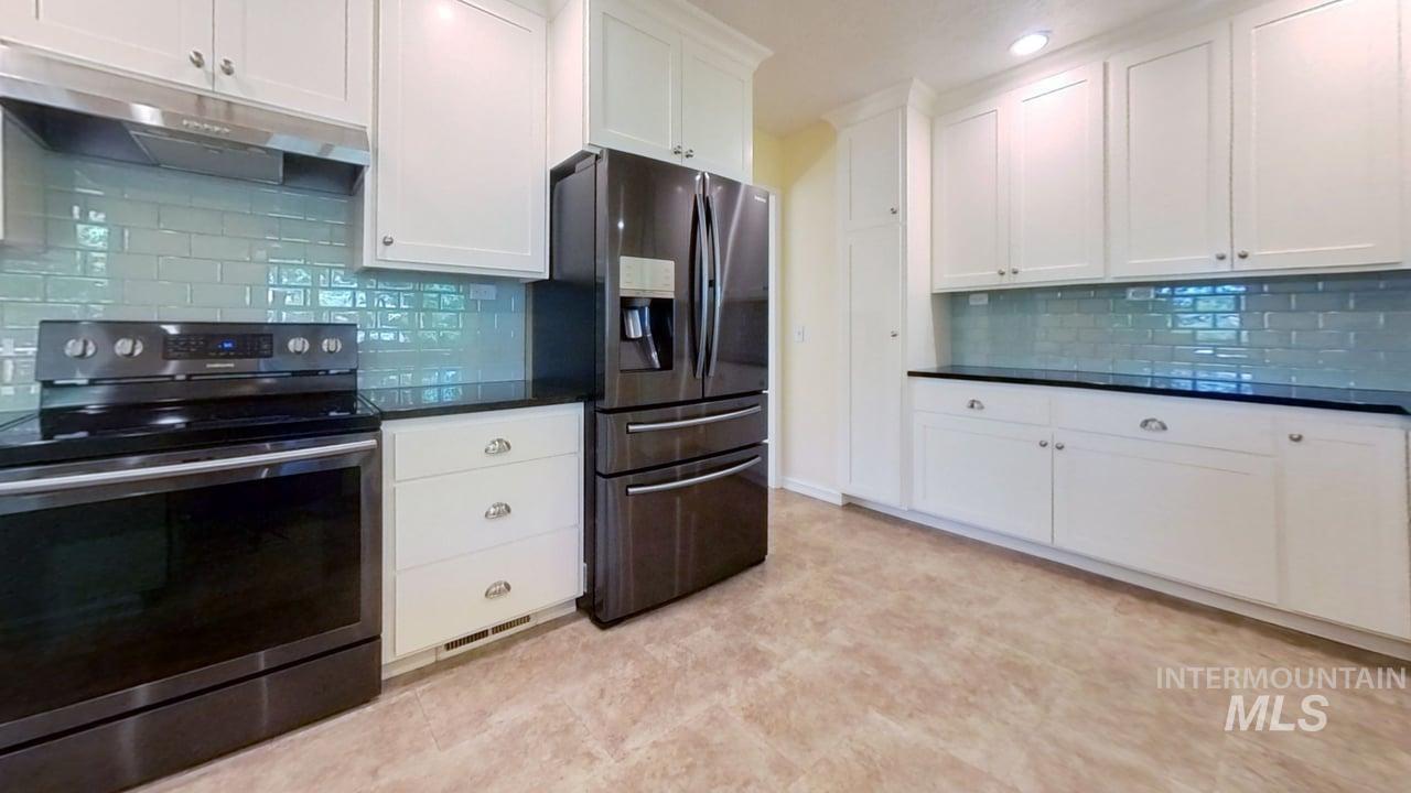 Kitchen featuring electric range oven, stainless steel fridge with ice dispenser, extractor fan, dark countertops, and decorative backsplash