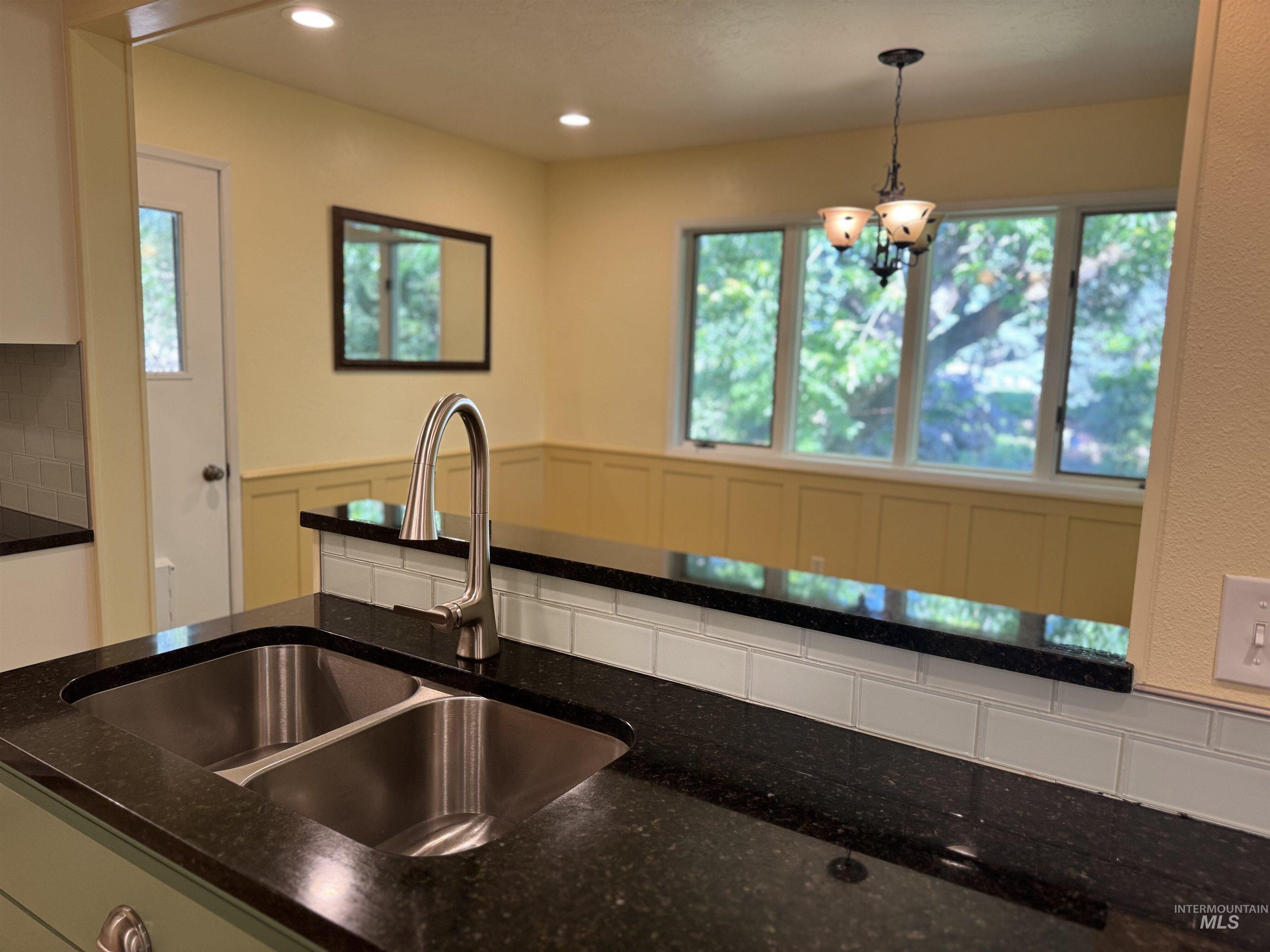 Kitchen featuring a chandelier, pendant lighting, dark stone counters, a wainscoted wall, and backsplash
