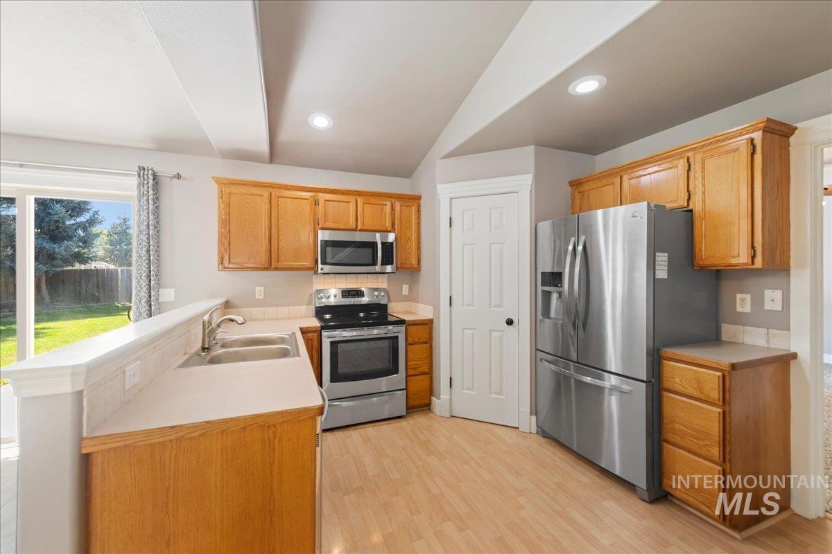 Kitchen with appliances with stainless steel finishes, light wood-style flooring, a peninsula, light countertops, and recessed lighting