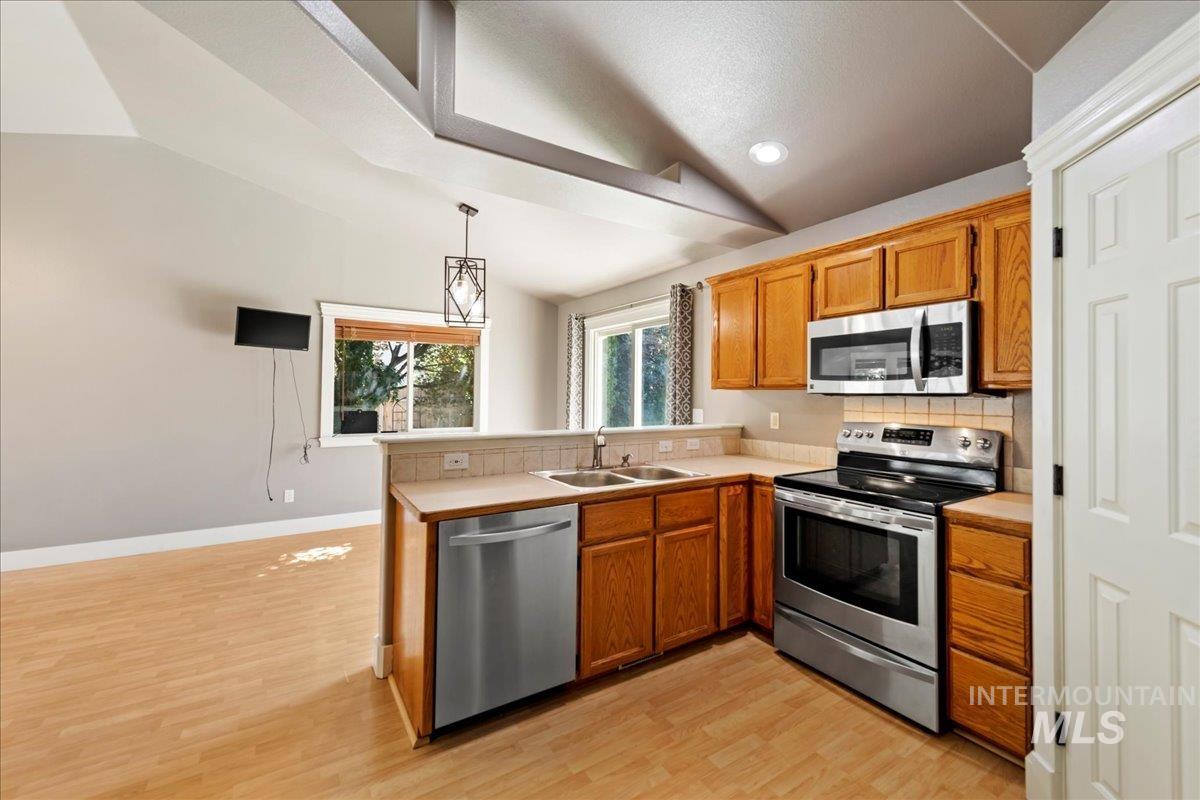 Kitchen featuring appliances with stainless steel finishes, a peninsula, lofted ceiling, brown cabinets, and light countertops